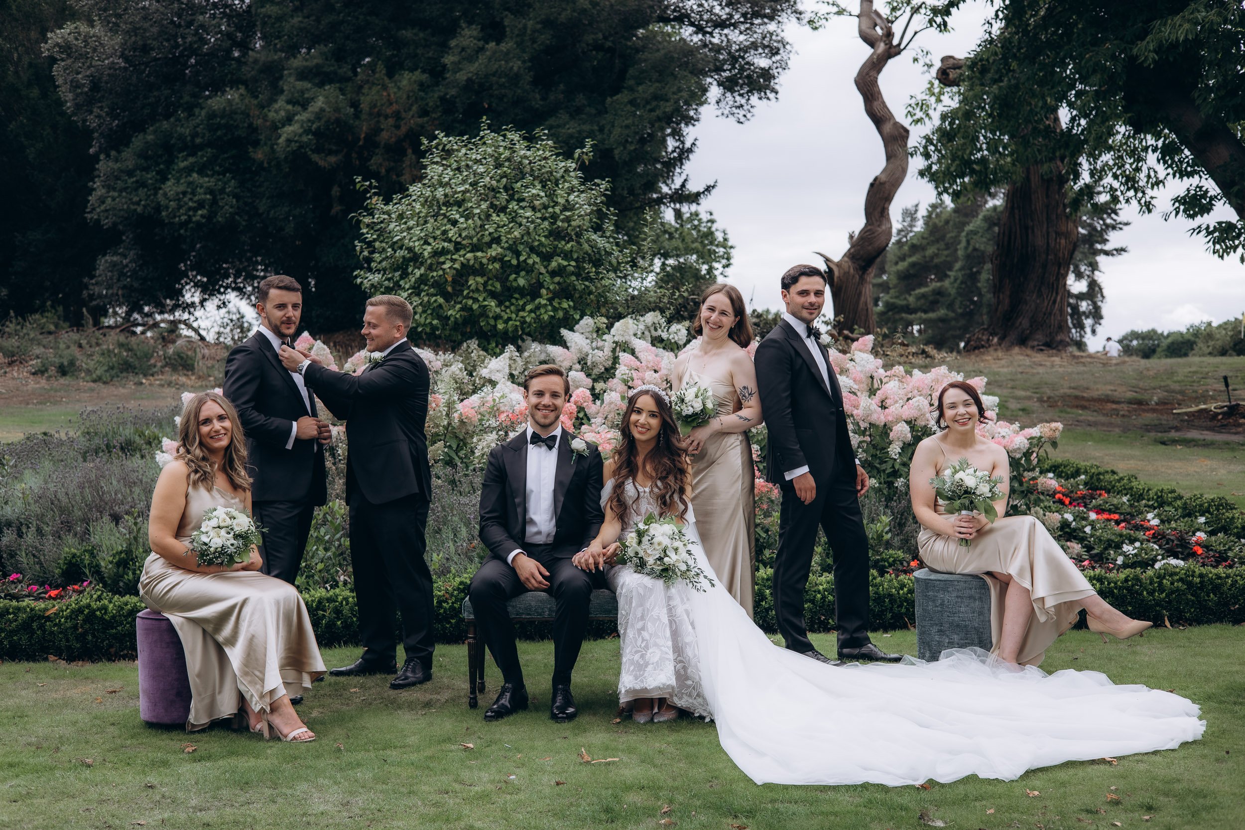 A modern and editorial-style group portrait of the wedding party posing in a lush, green London park setting.