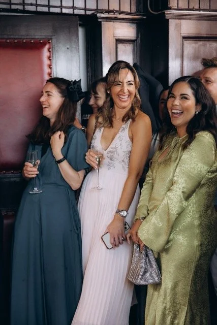  Three women sharing a joyful laugh at a London wedding reception — genuine candid moment captured in documentary style by Lusy Klintsova Photography 
