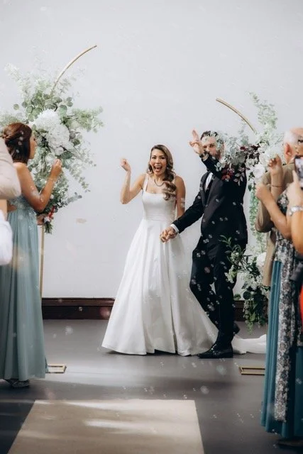 Bride and groom celebrating under the floral arch as guests throw confetti