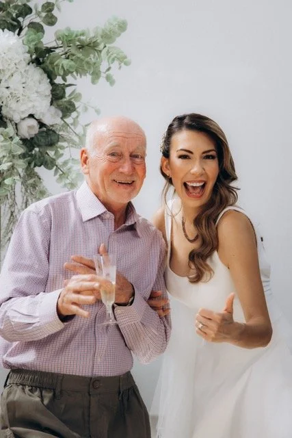  bride and his dad laughing together, both holding glasses of champagne