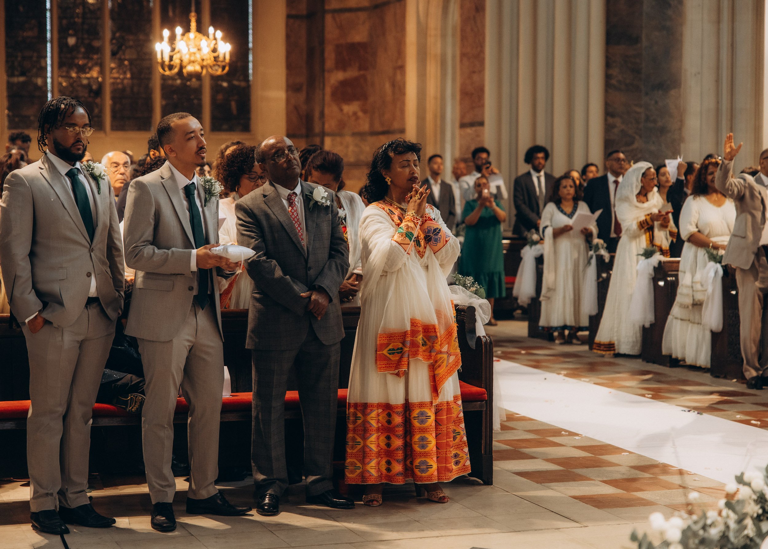 An environmental shot capturing the wedding congregation from behind, with a focus on guests and family members wearing beautiful, colorful traditional Ethiopian traditional white and gold ceremonial attire during a high-end cultural wedding in a Lon
