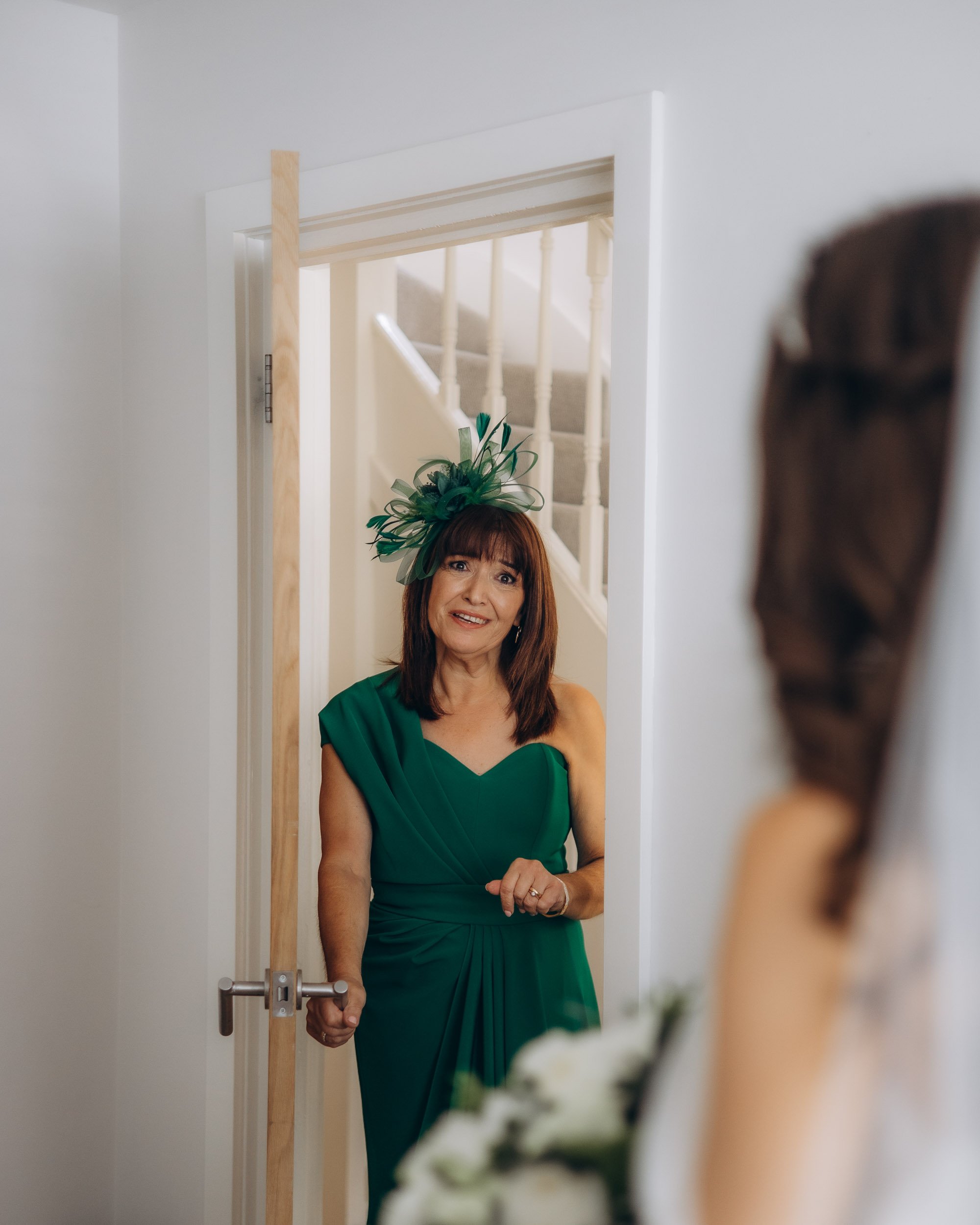 Touching candid moment of a mother of the bride in a green dress during wedding morning preparations in London.