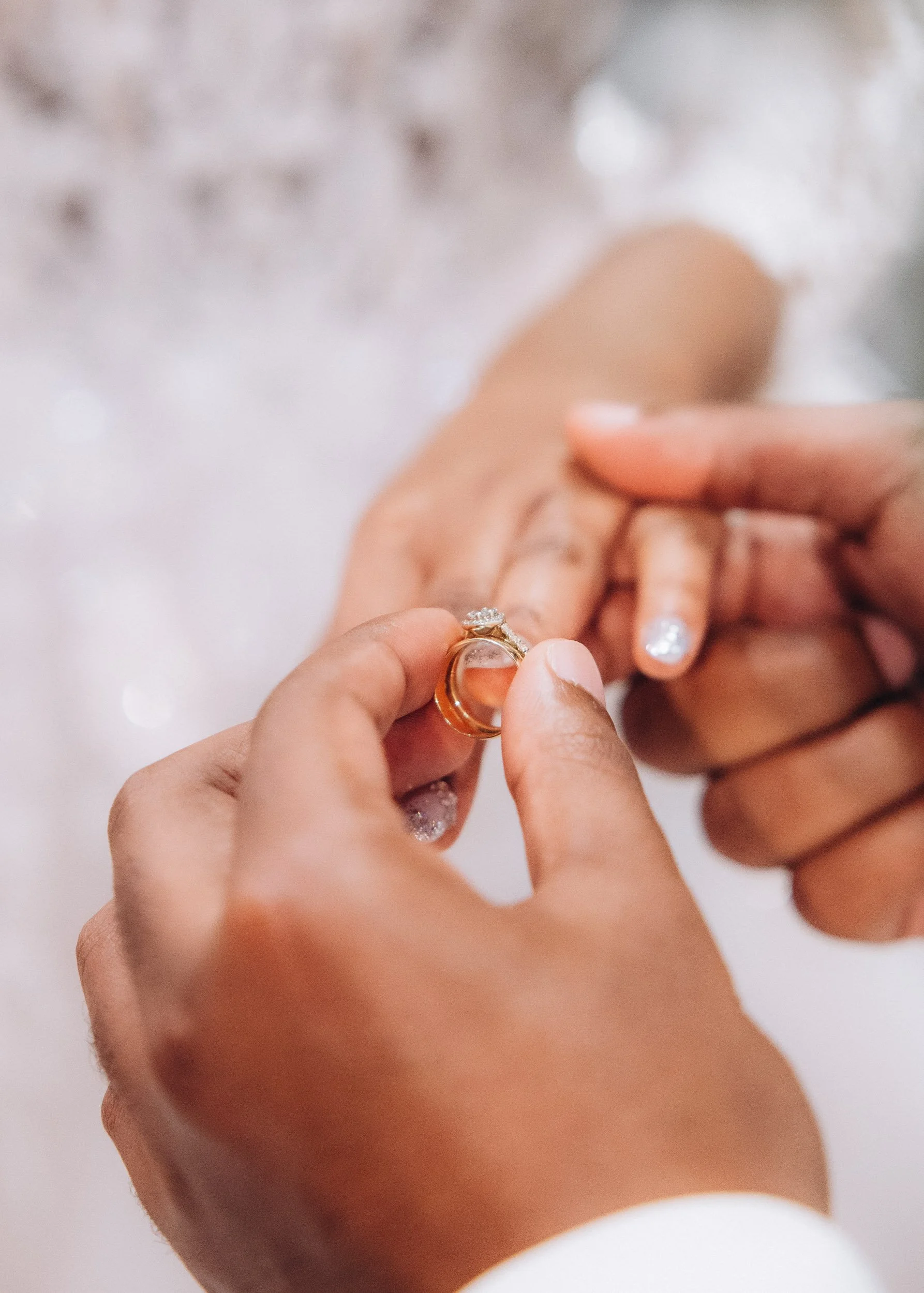 Extreme close-up macro photography of the groom placing a gold wedding band on the bride's finger, focusing on the detail of the rings and the moment.