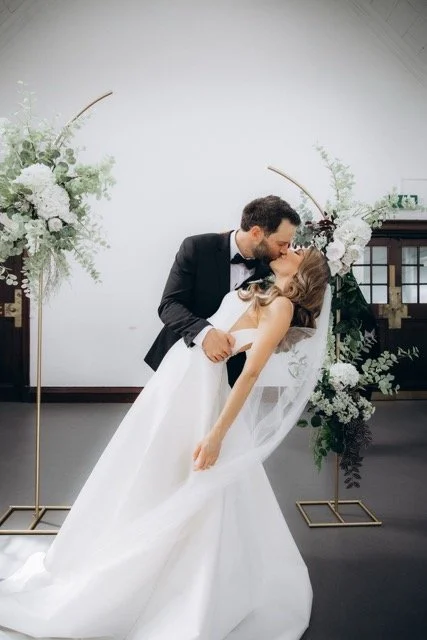 Groom dipping the bride for a kiss in front of the ceremony floral arch