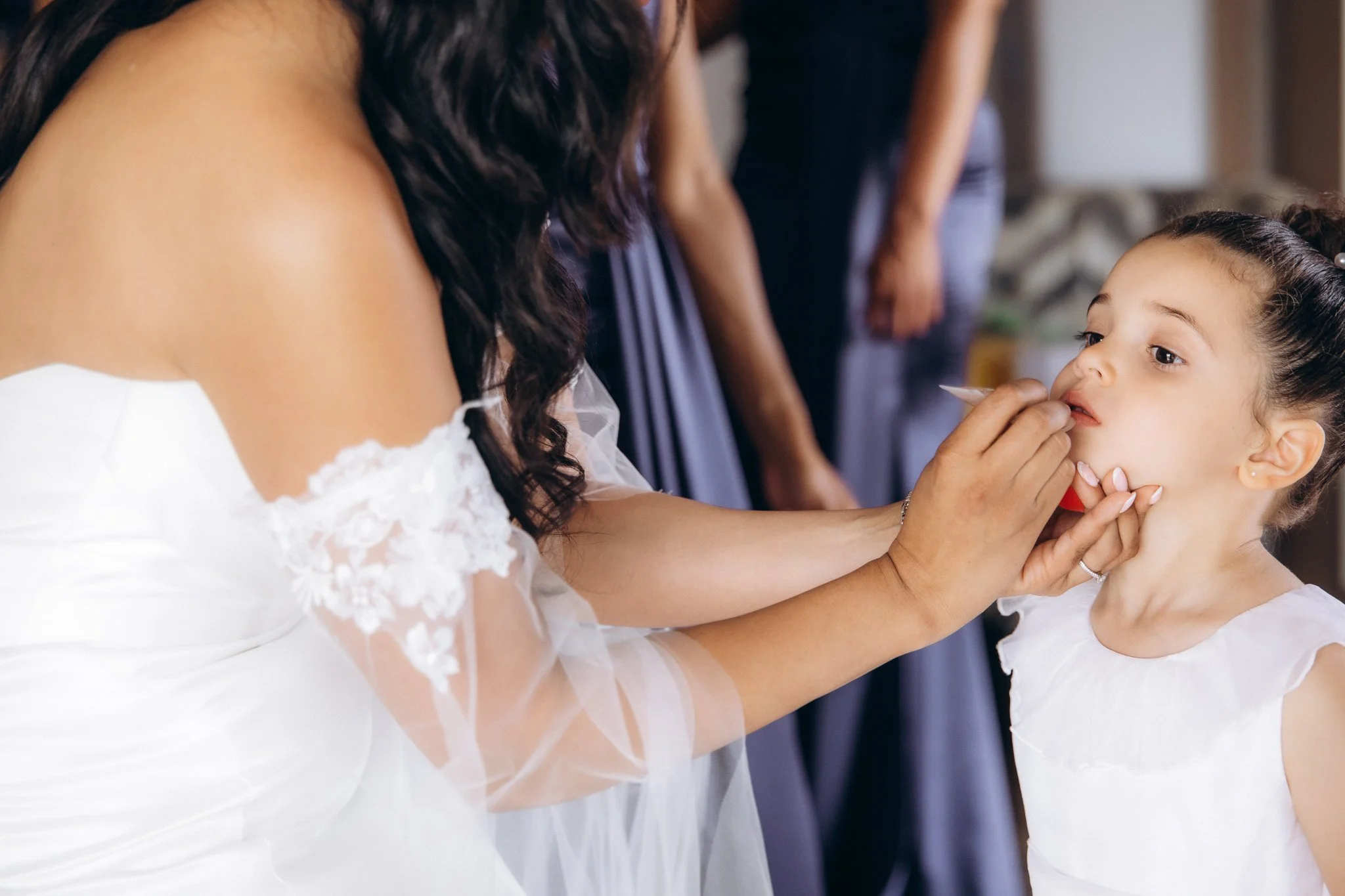 Close-up of a bride's lace sleeve and shoulder detail with a bridesmaid's hands nearby