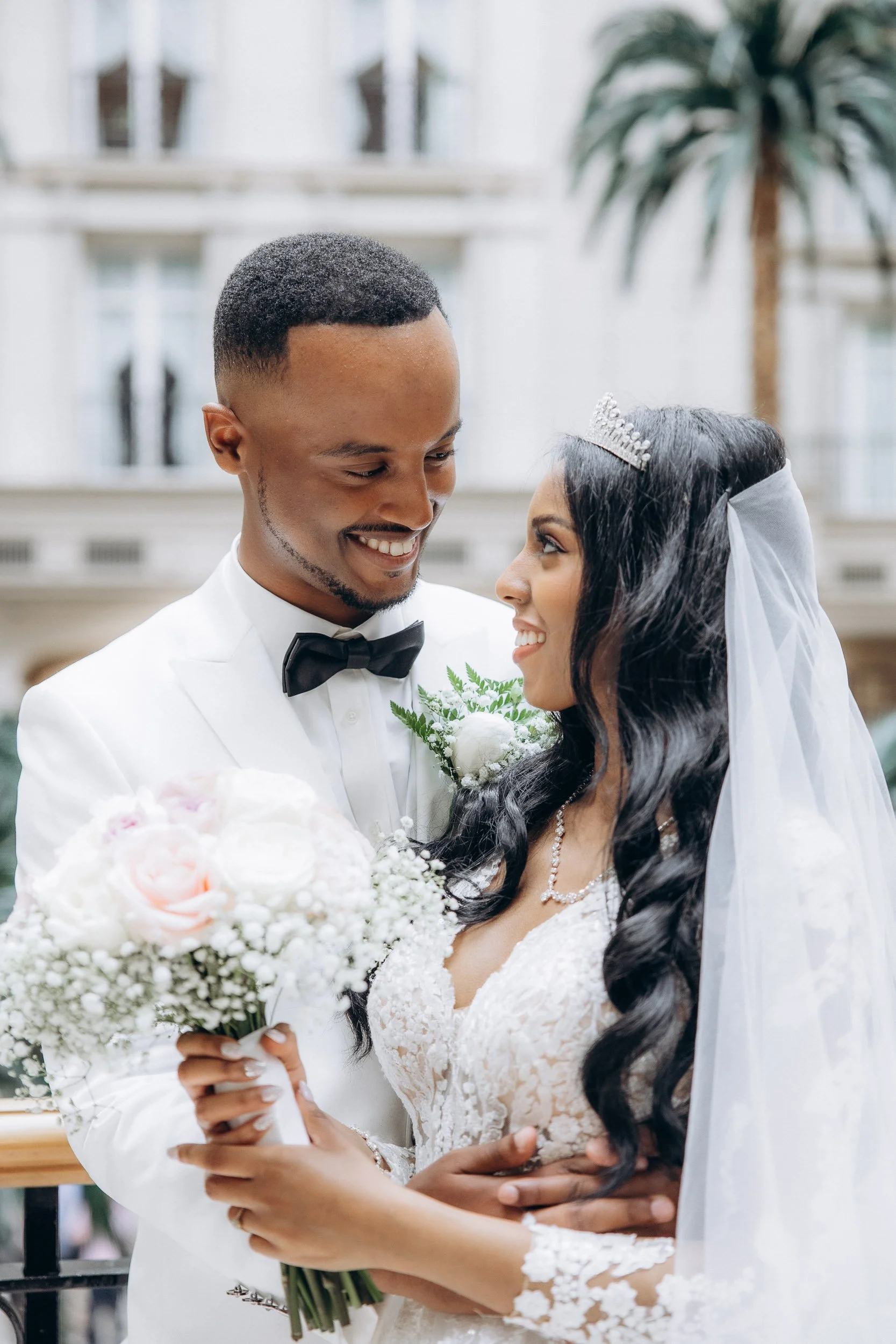 Candid portrait of a smiling Black bride in an elaborate gown and a Black groom in a white tuxedo, sharing a joyful and personal moment of laughter. High-quality wedding photography for premium clients in London.