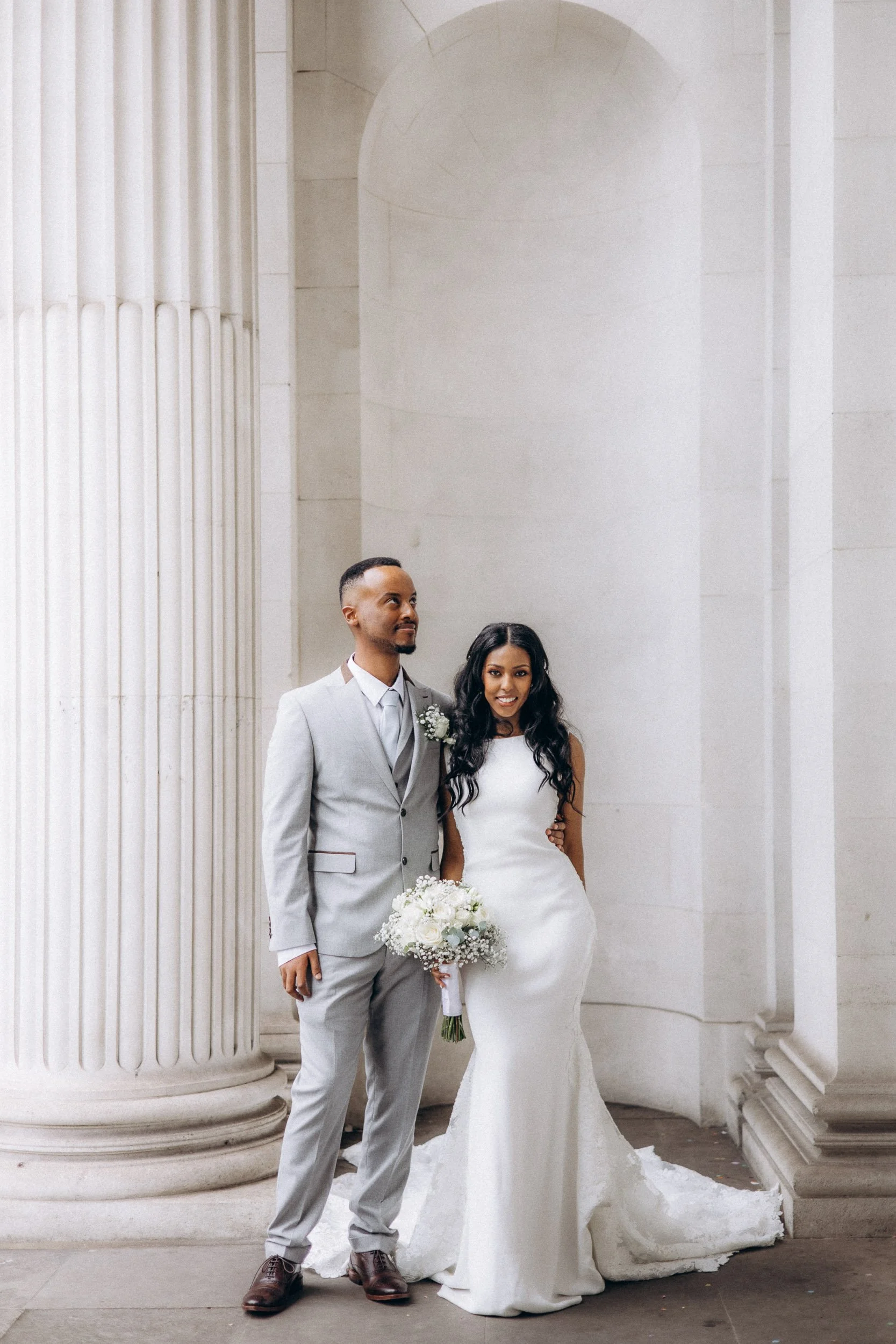Bride and groom standing beneath the curved stone colonnade at Old Marylebone Town Hall