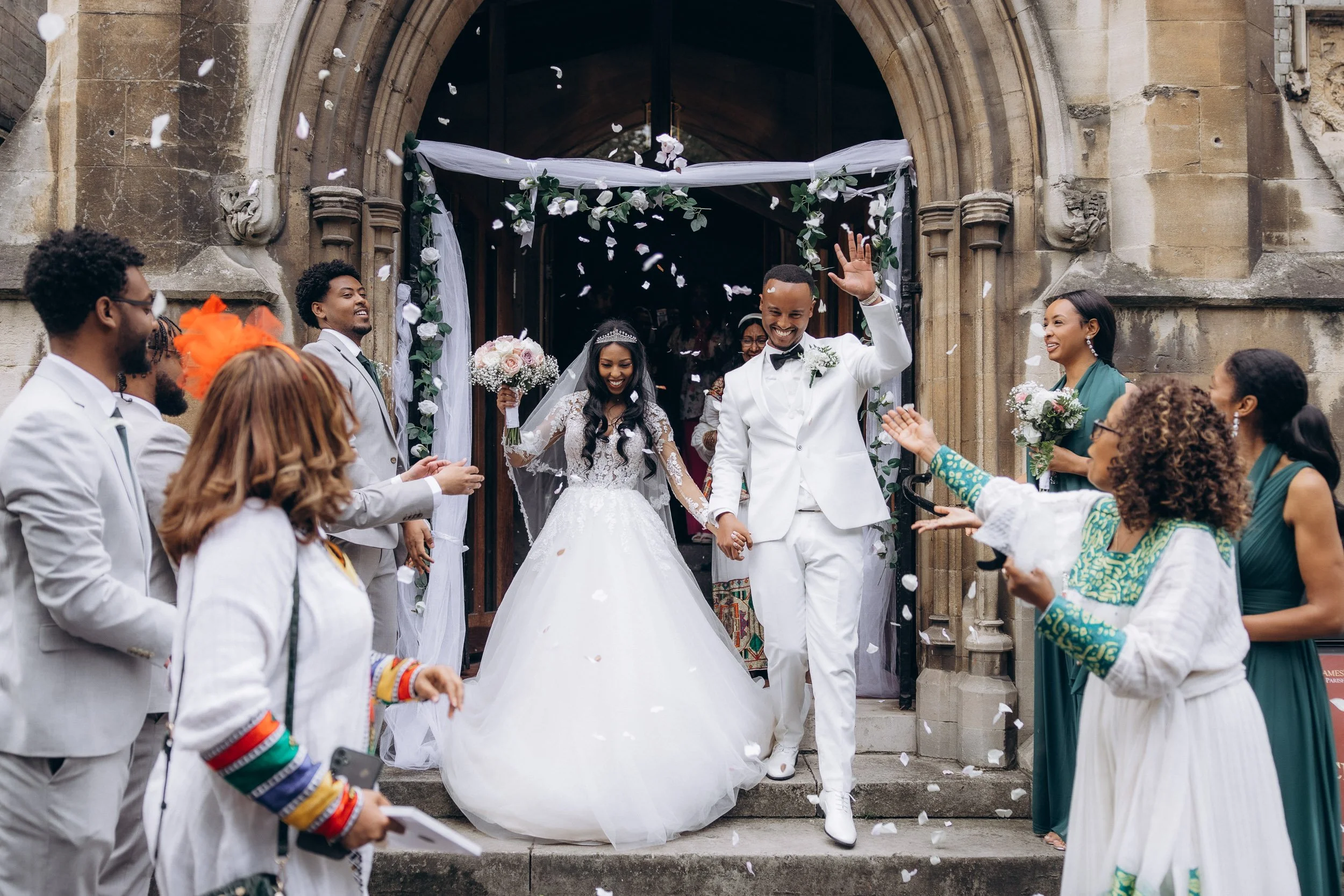 Joyful bride and groom walking out of a stone church entrance during a confetti exit; high-energy documentary wedding photography in London.
