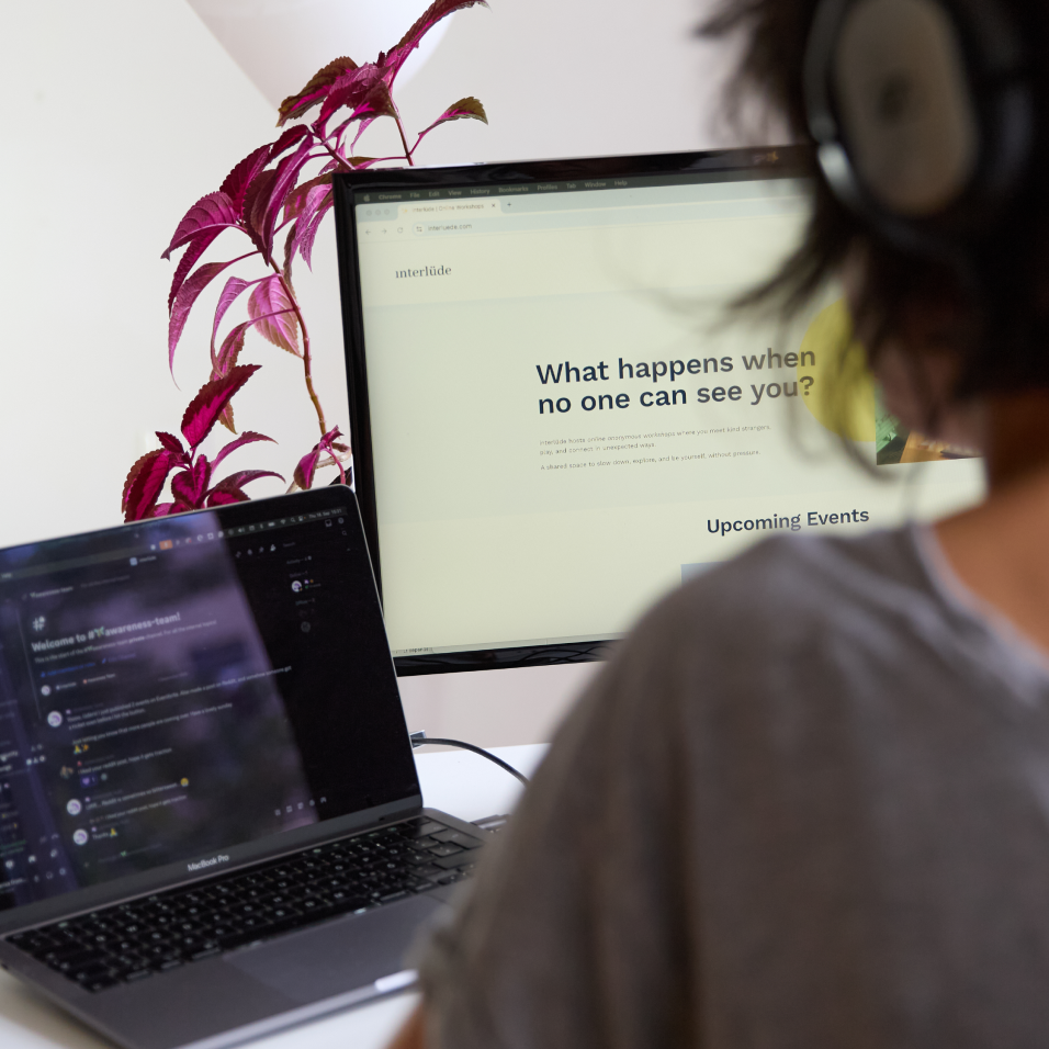 A person working at a desk with two monitors, one displaying a website with the ‘What happens when no one can see you?’ title and the other showing a Discord server, where an audio session is going on.
