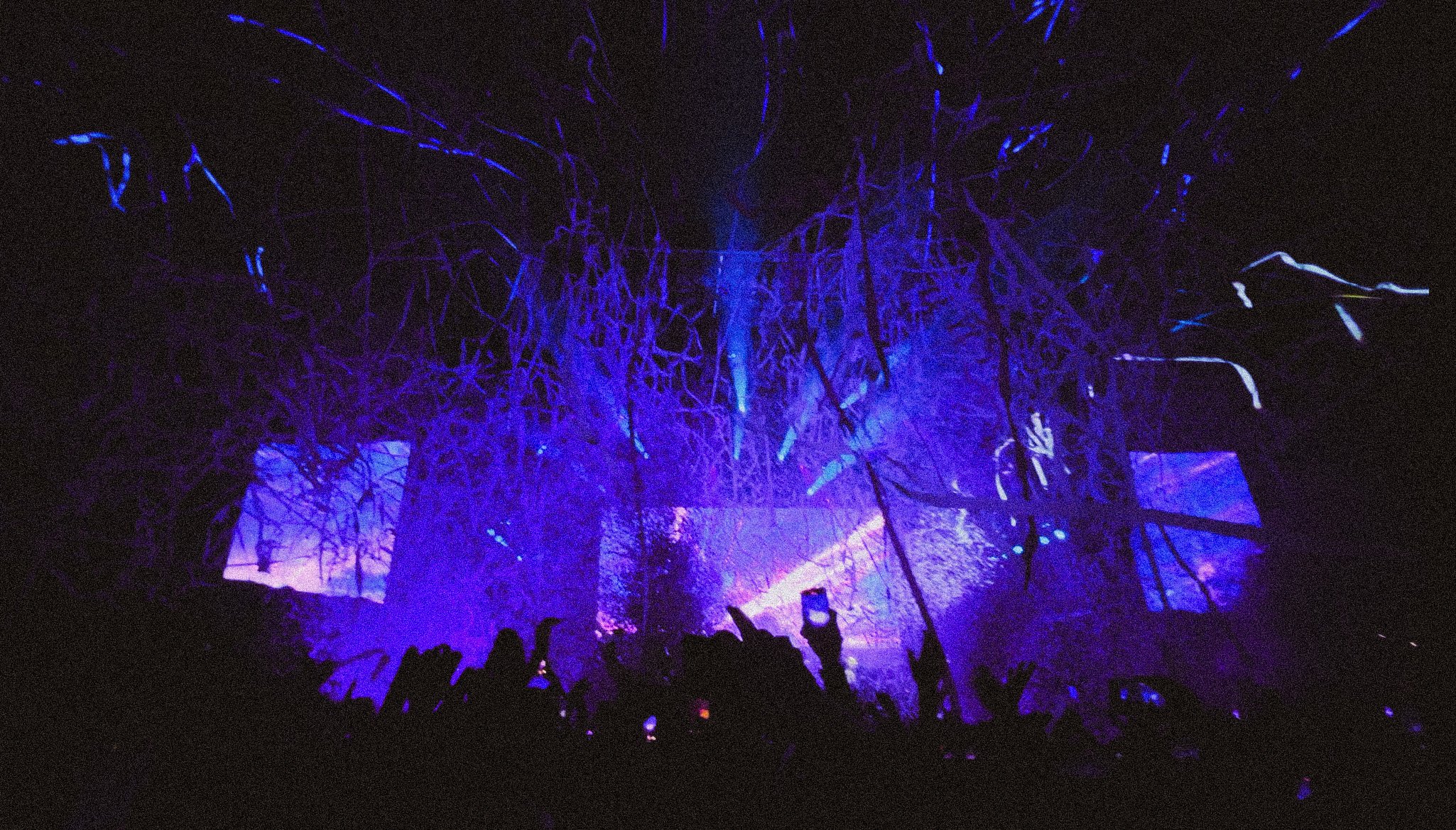 Dark scene of people at a concert or event with purple and blue lighting, and projected visuals on background screens. Sam Fender, TRNSMT Festival