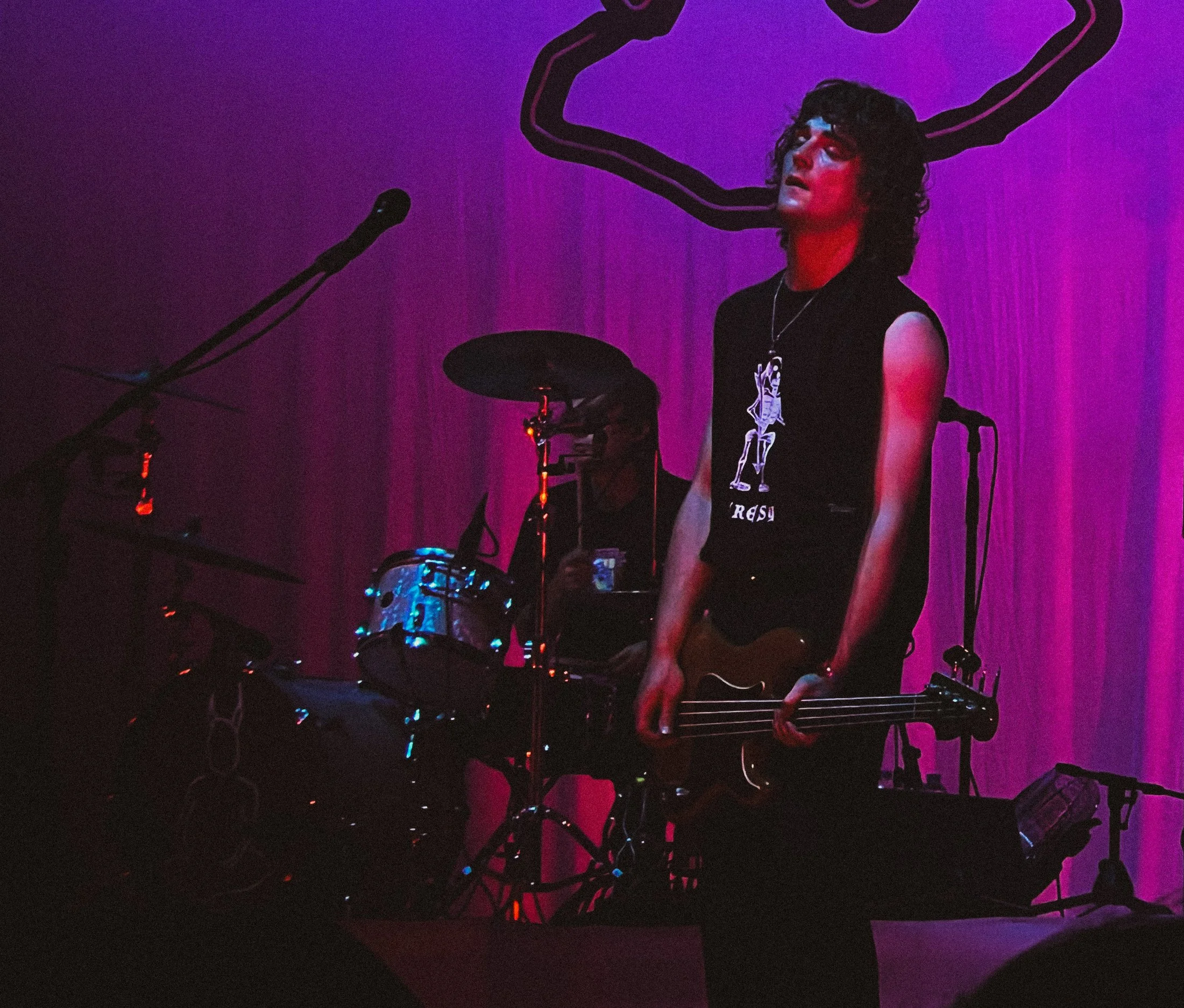 Musician playing guitar and singing on stage with purple curtains and neon wall outline behind him