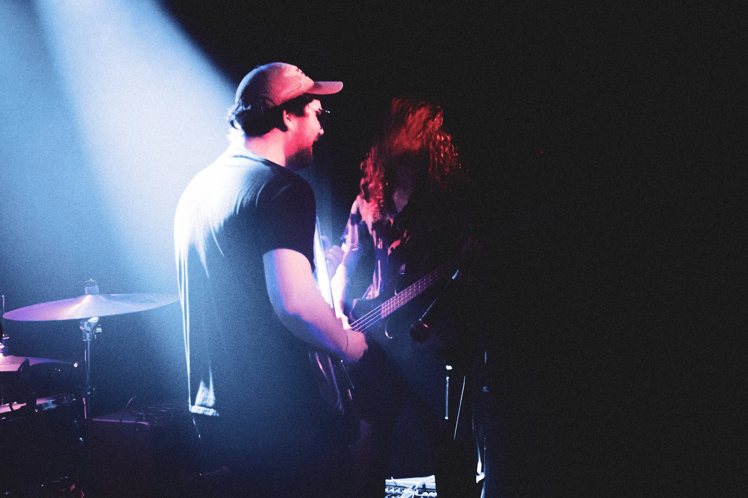 Two musicians performing on stage, one playing guitar and the other unseen, with stage lights creating a moody atmosphere.