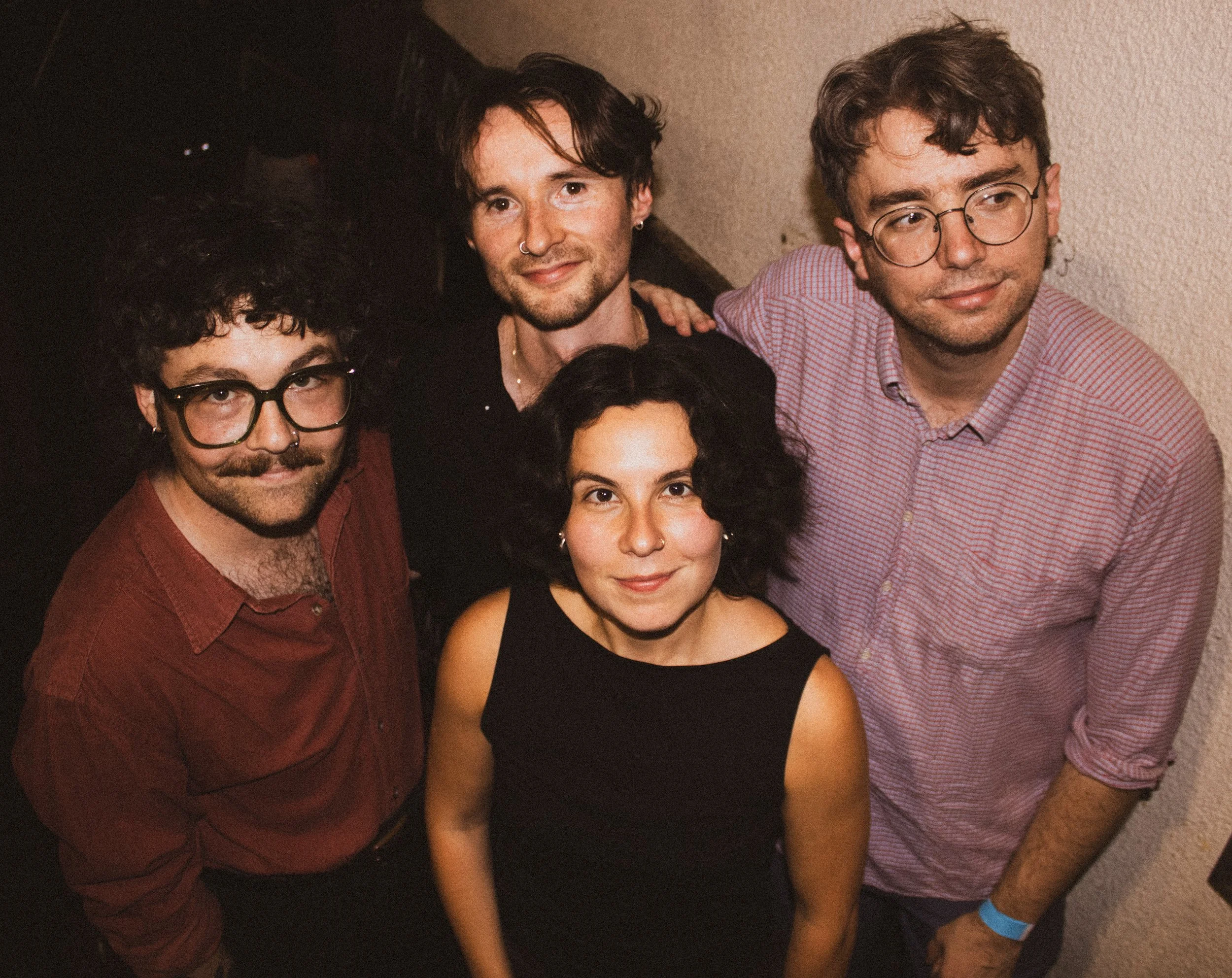 Group of five young adults standing close together indoors, smiling and looking at the camera.