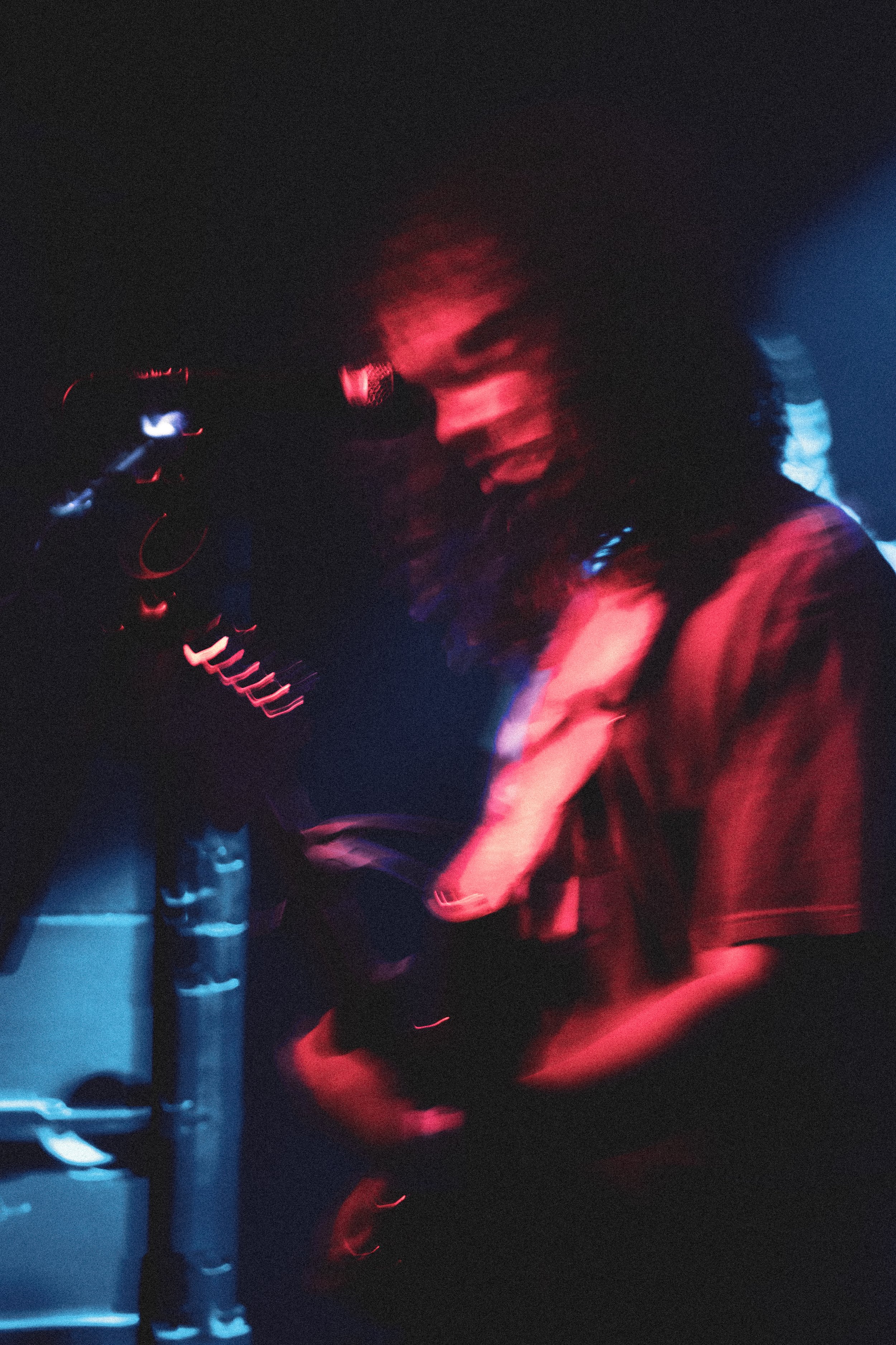 A person with curly hair in a dark environment illuminated by red and blue lights, appearing to move or dance.