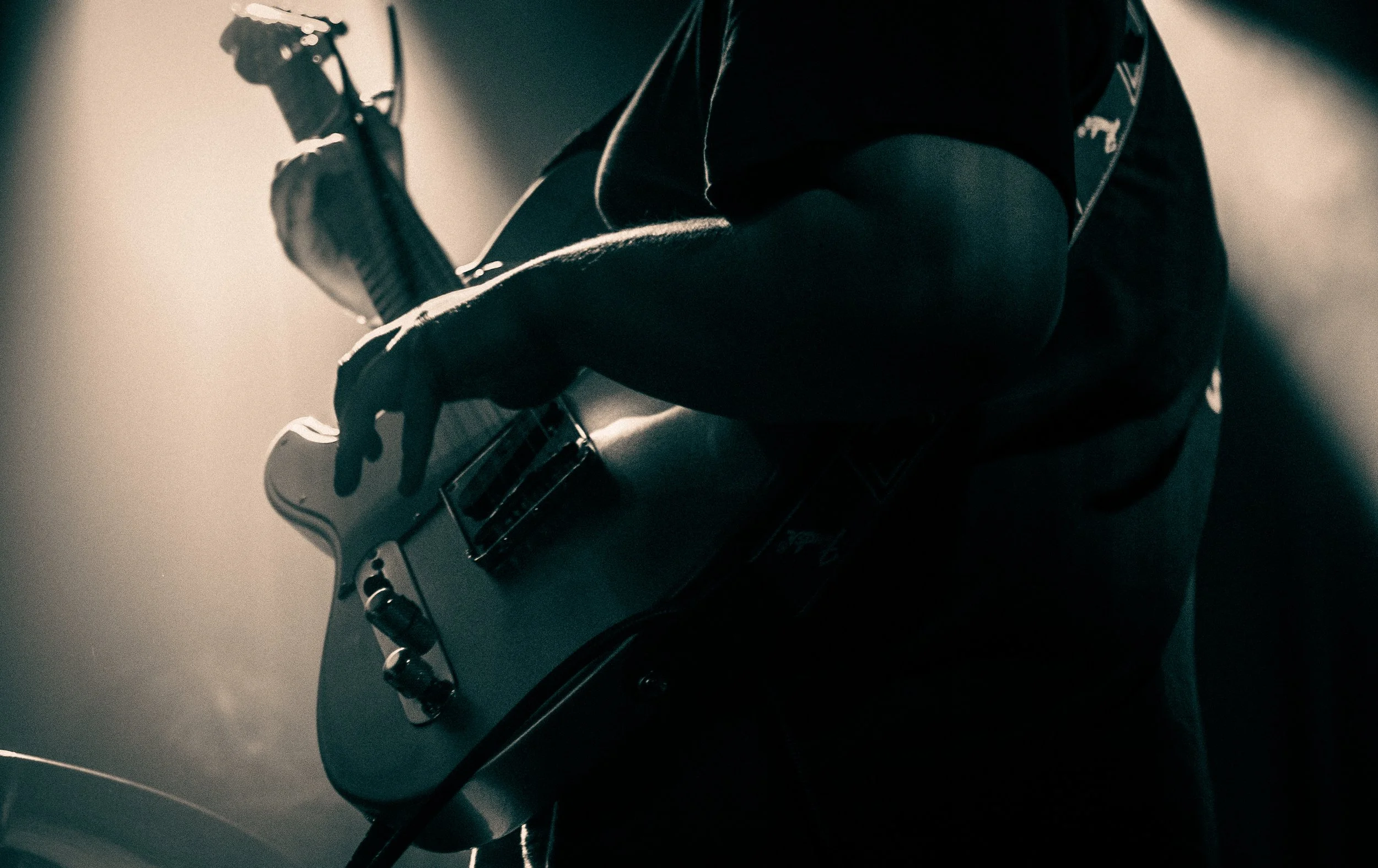 Person playing electric guitar in low light, emphasizing hands and guitar.