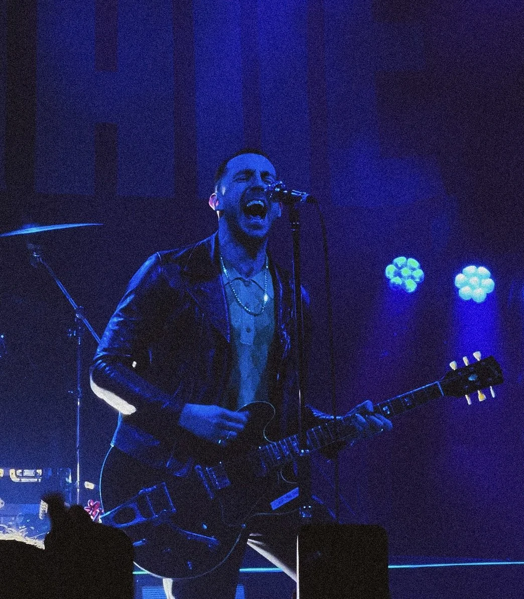 Musician singing and playing an electric guitar on stage with blue lighting.