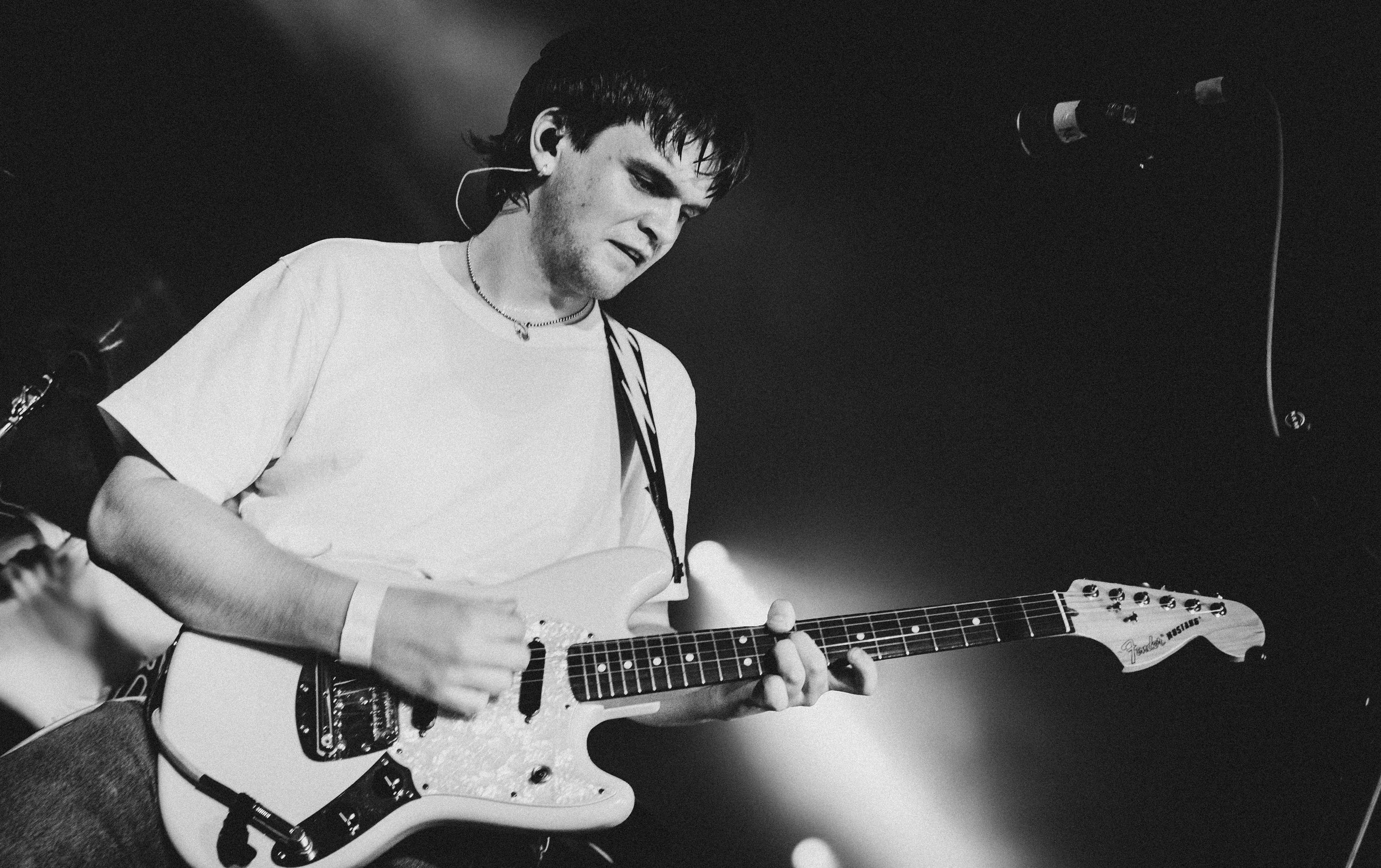 A young male guitarist performing on stage with enthusiasm, holding a Fender electric guitar, under dramatic stage lighting.