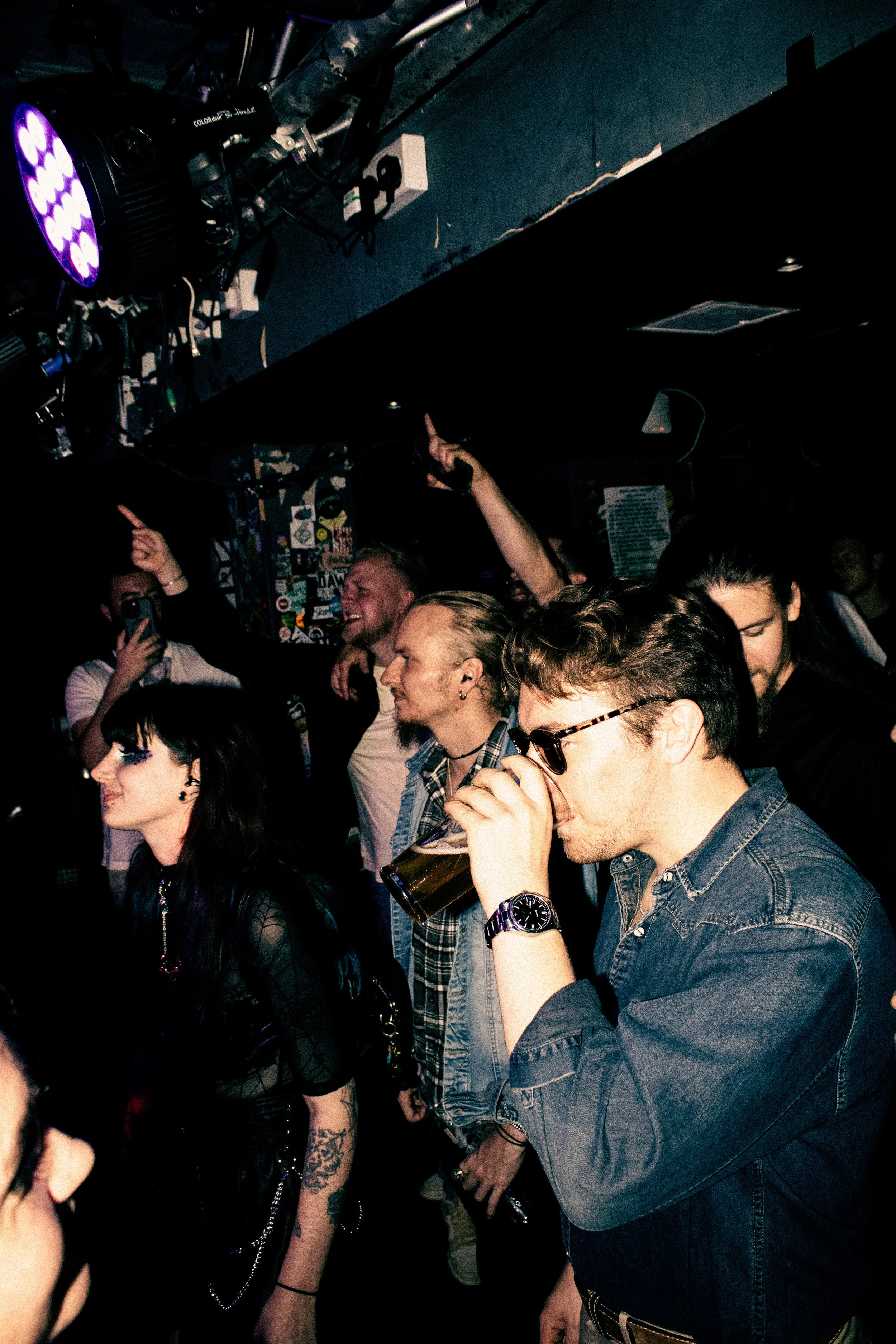 People enjoying a night out at a club, some dancing and others drinking, in a dimly lit venue with colorful lights.
