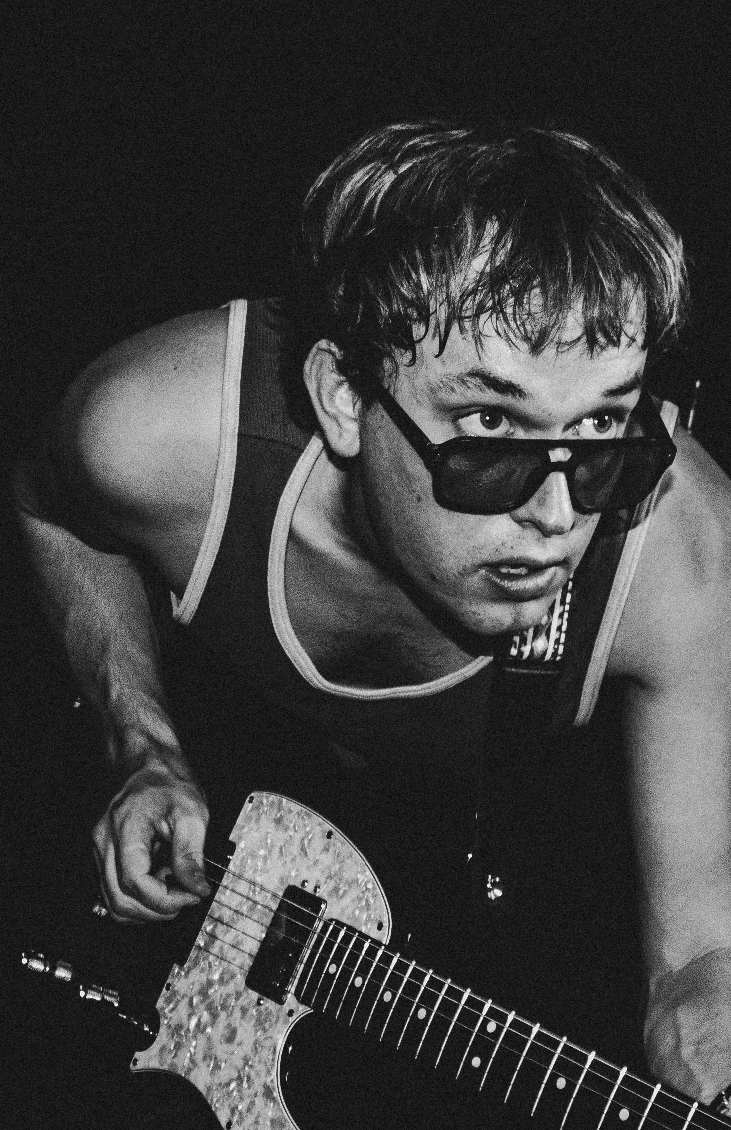 Black and white photo of a young man wearing sunglasses, holding an electric guitar, looking upward with an intense expression.
