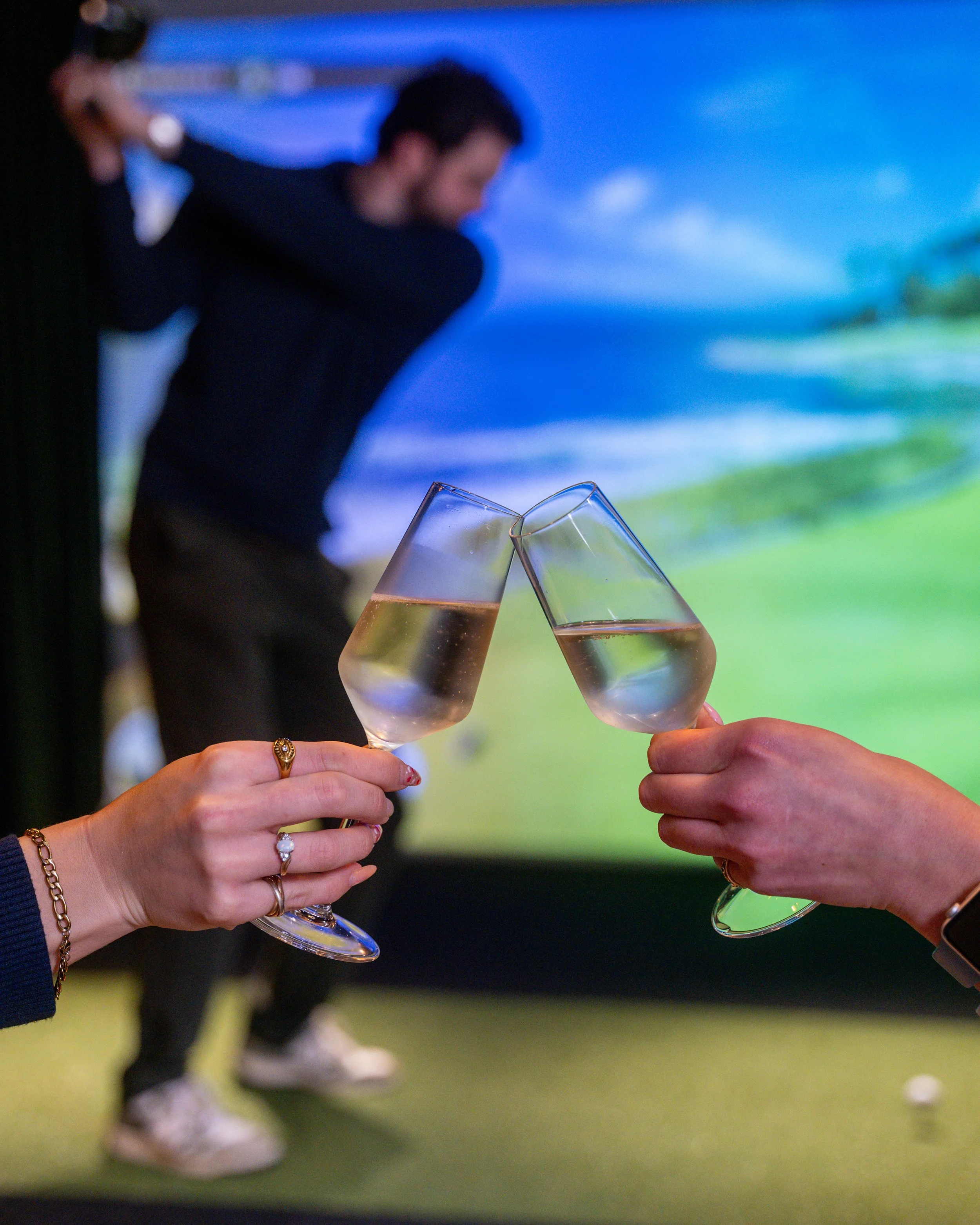 Two people toasting with glasses of champagne at a golf simulator.