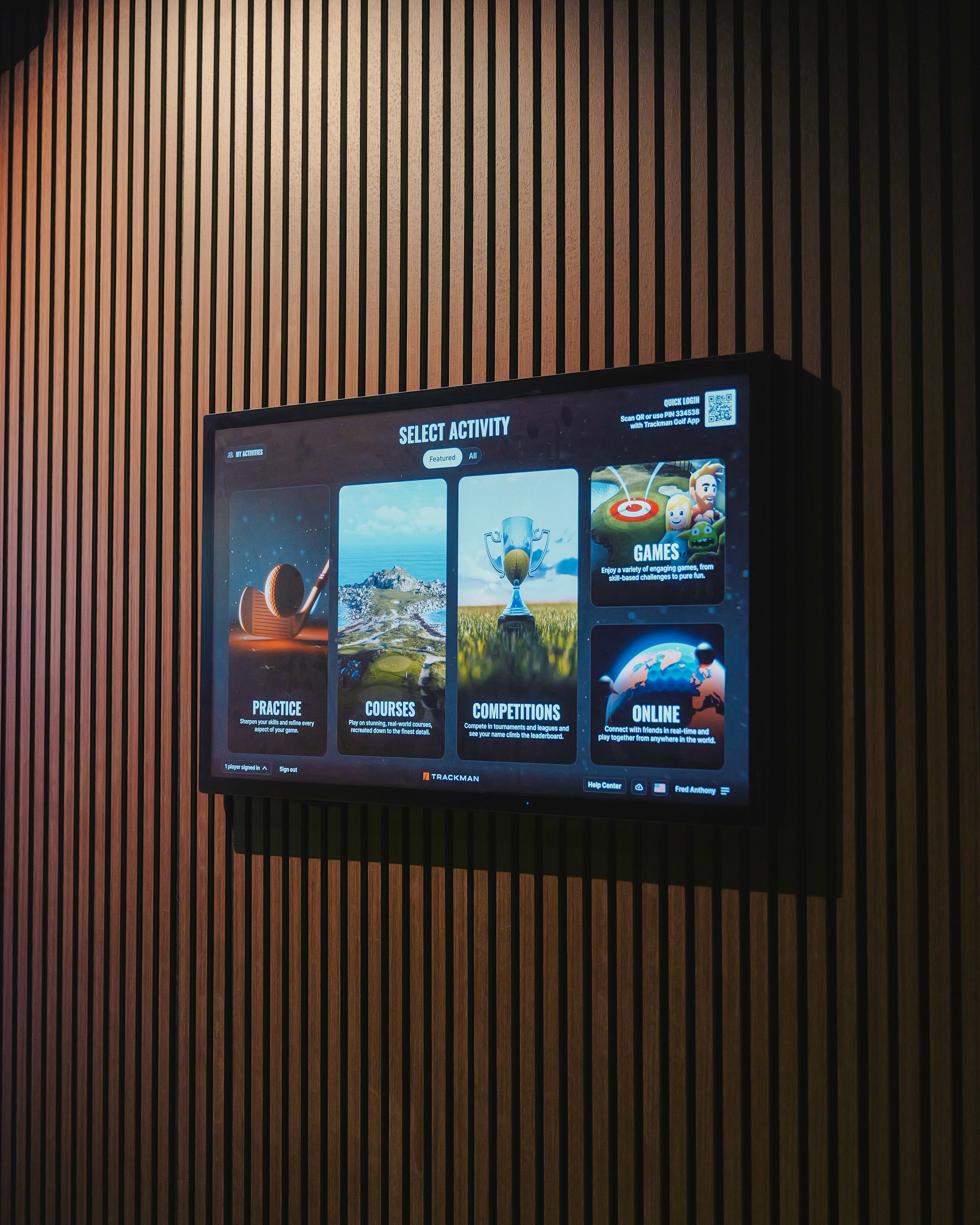 Digital screen showing golf activities and options, mounted on a wood-paneled wall.
