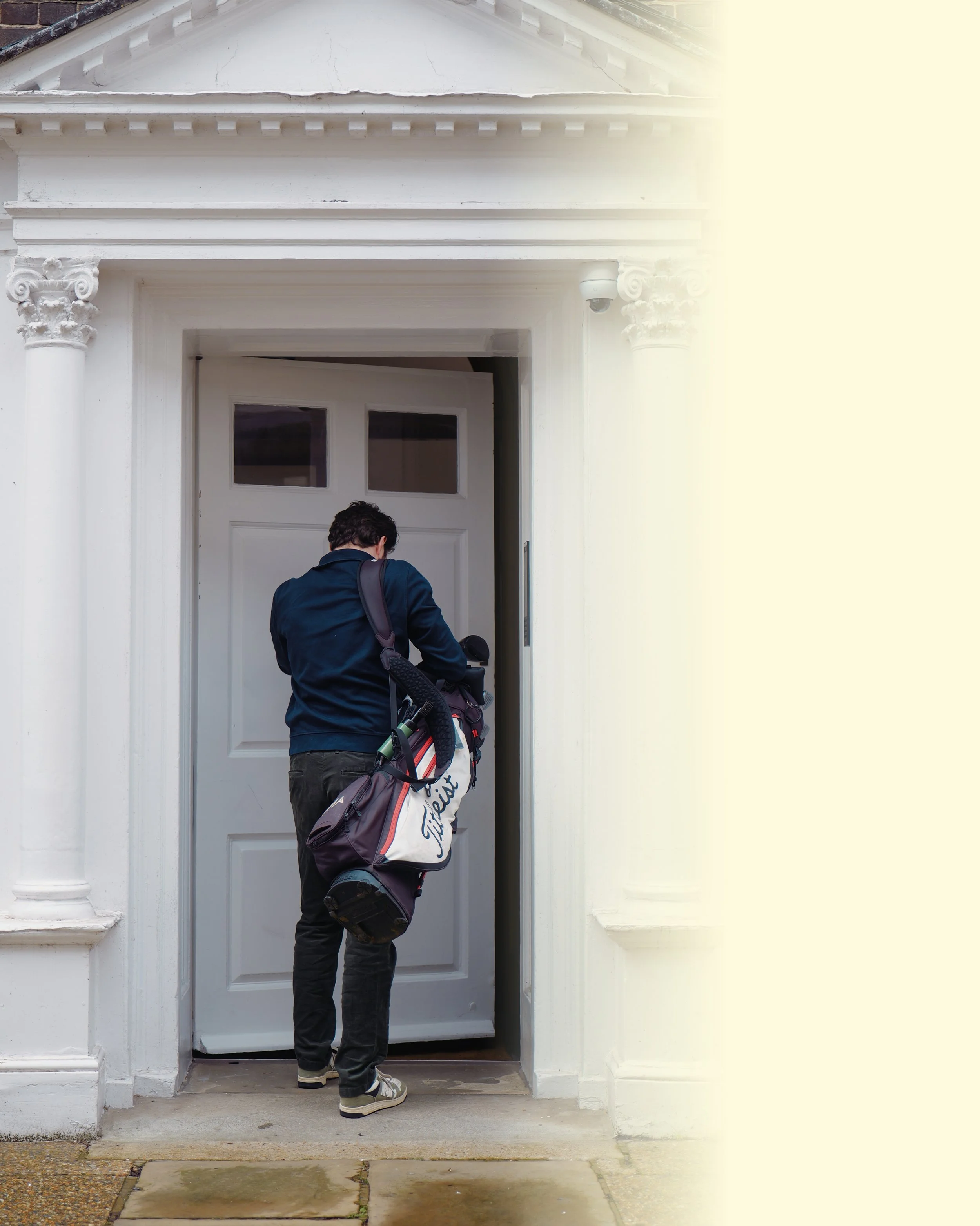 Person with a golf bag entering a white house door.