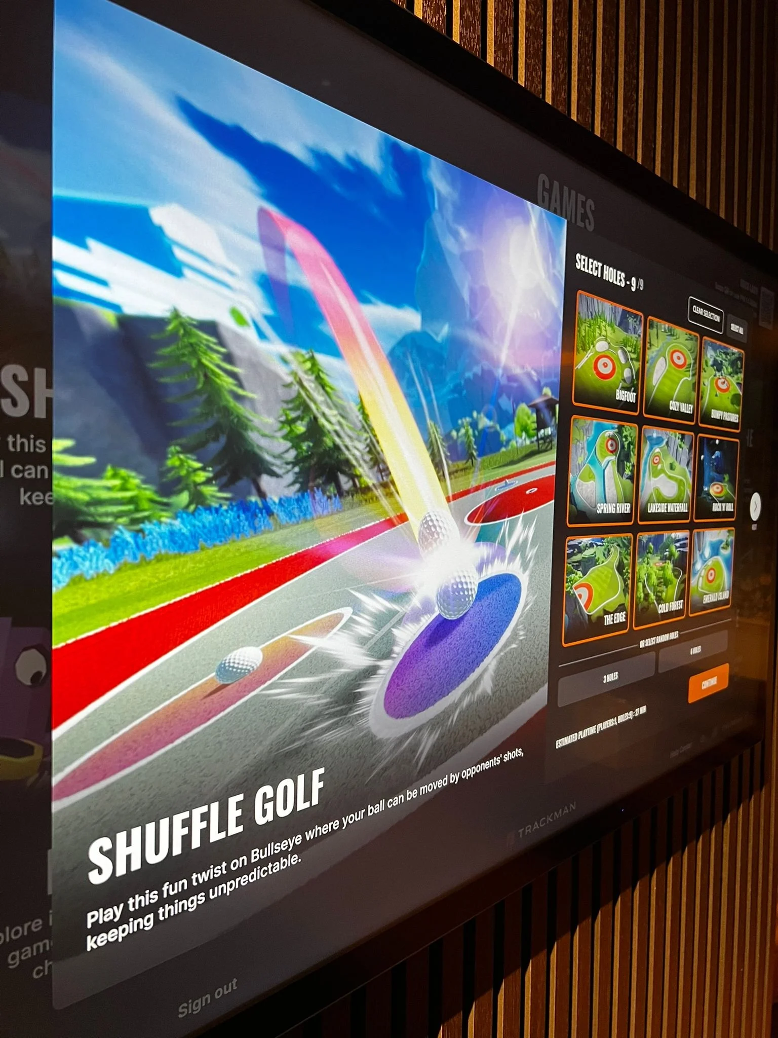 On a touchscreen, a virtual golf game showing balls being hit towards a hole in a colorful, animated golf course landscape.