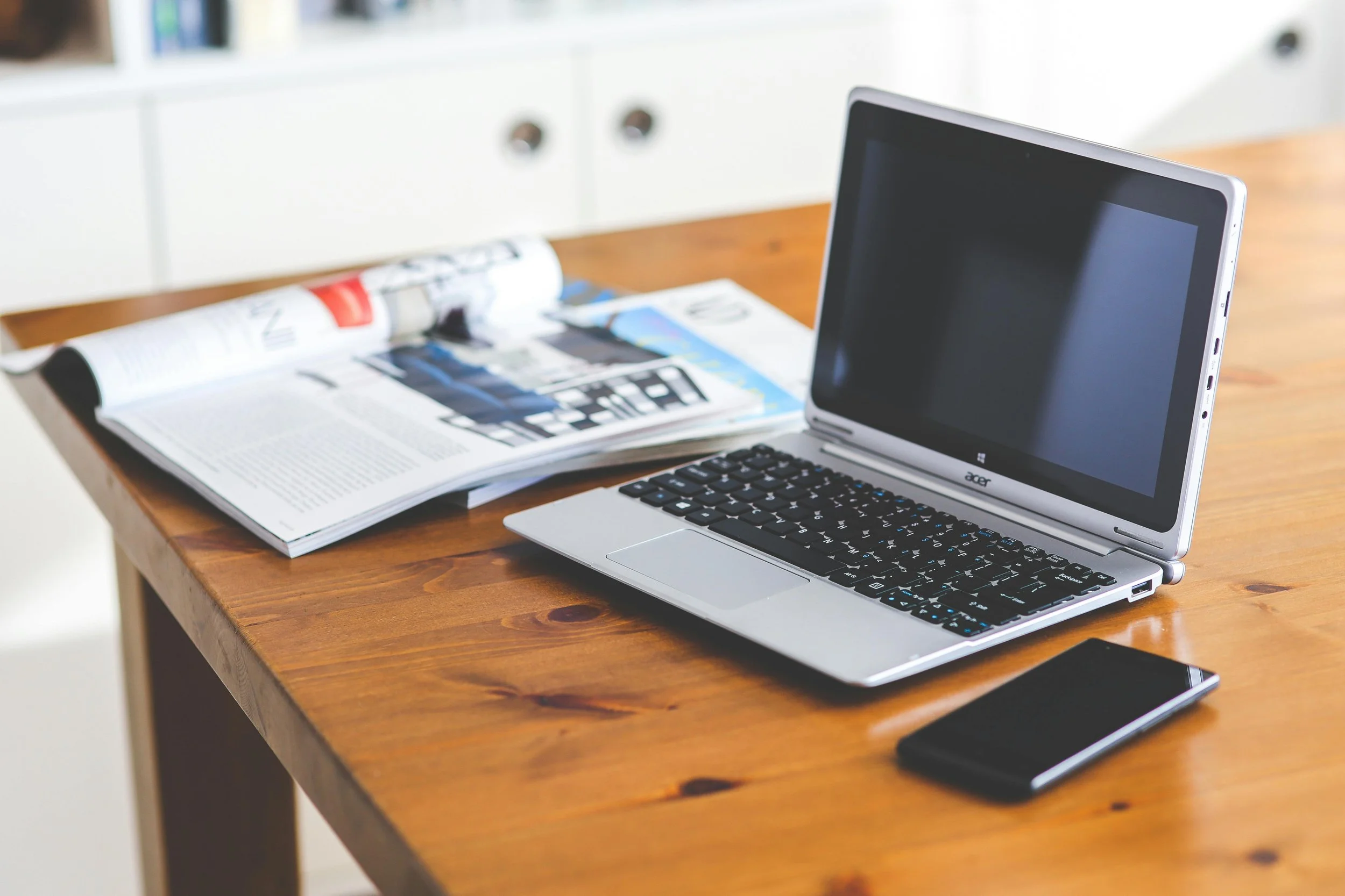 A wooden table with an open magazine, an Acer laptop, and a smartphone placed on it.