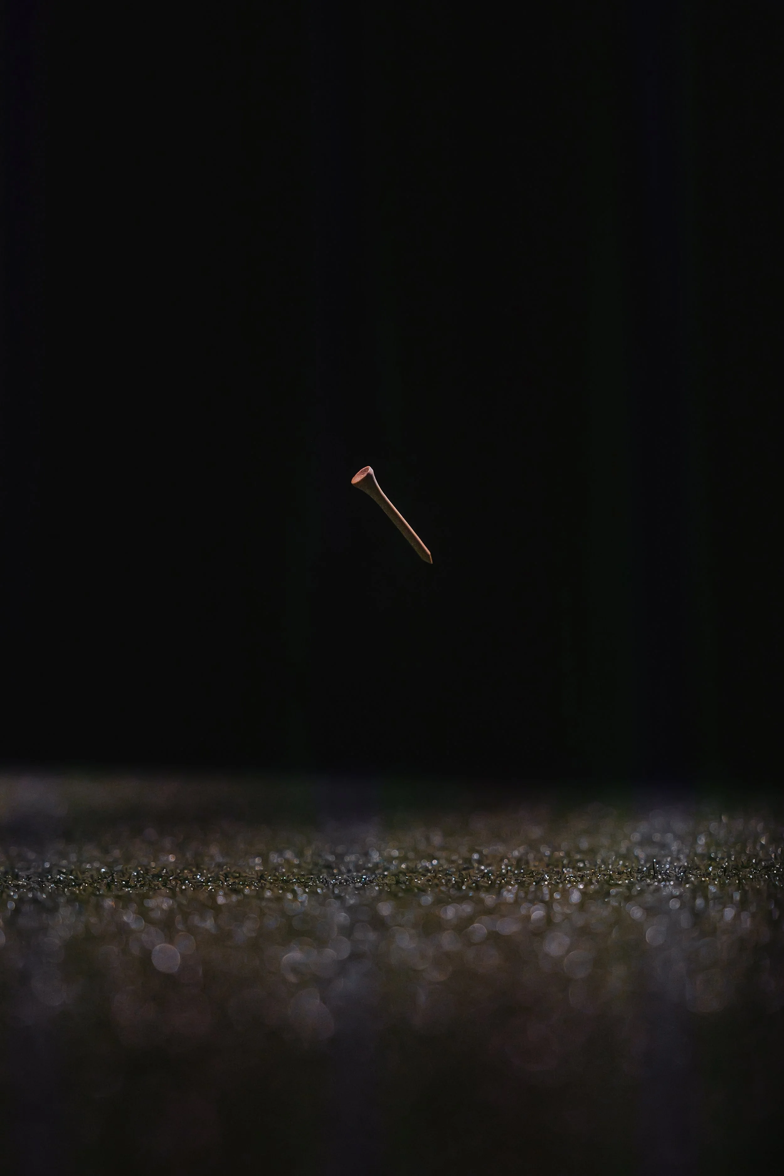 A nail falling through the air over a textured surface, with a dark background.