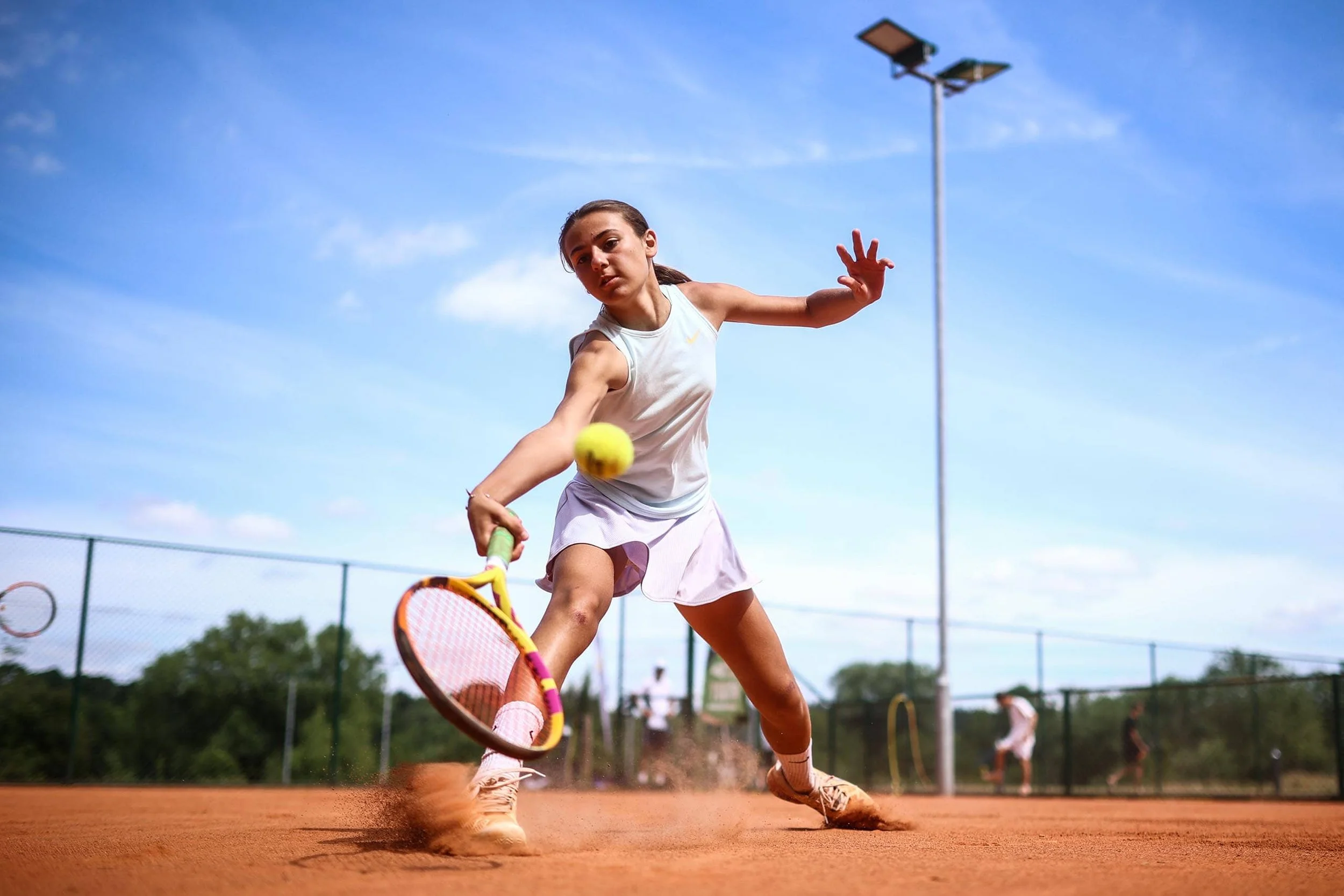 Girl reaching to return ball on sand tennis court