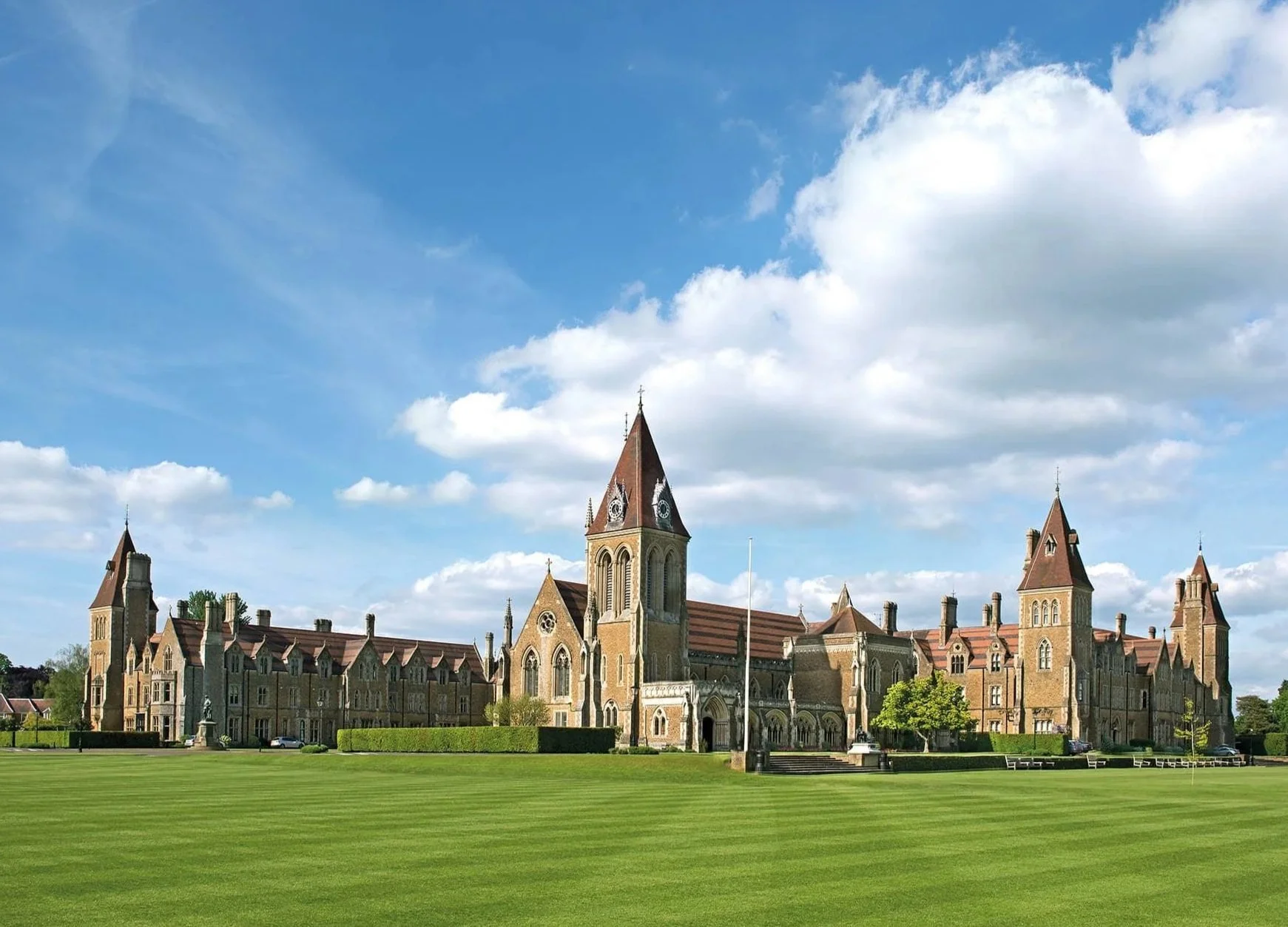 Una histórica iglesia de piedra con múltiples campanarios altos recortados contra un cielo parcialmente nublado, rodeada por un césped verde bien cuidado y algunos árboles.