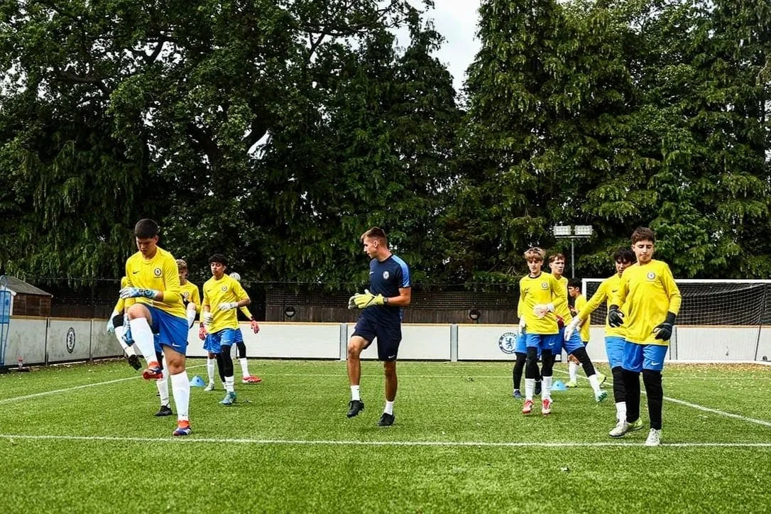 Equipo juvenil de fútbol entrenando en un campo con porterías y árboles al fondo.