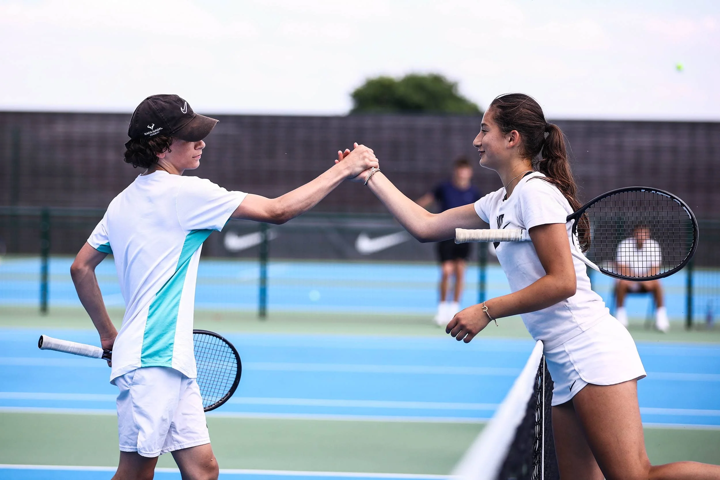 Mädchen und Junge beim Nike Tennis Camp geben sich über dem Netz die Hand
