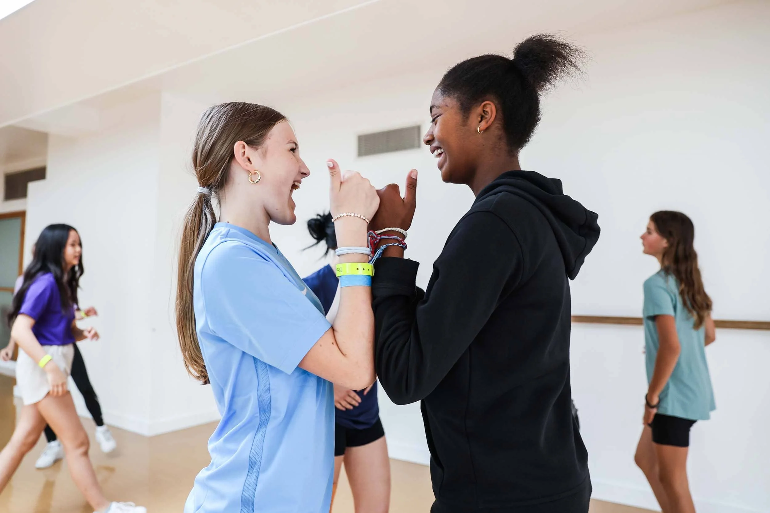 Two girls in dance studio laughing and holding hands
