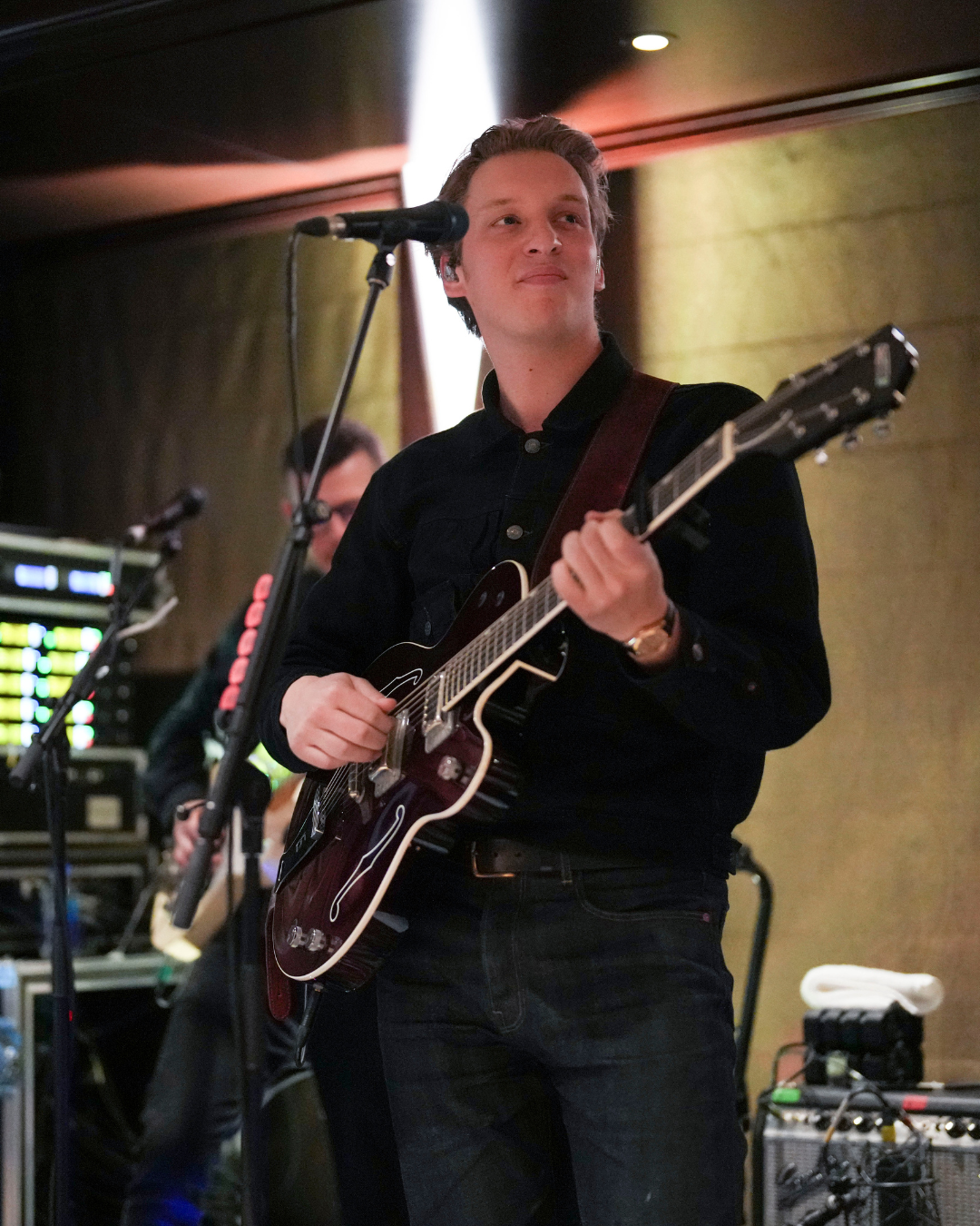 George Ezra playing an electric guitar and singing into a microphone during a live music performance.