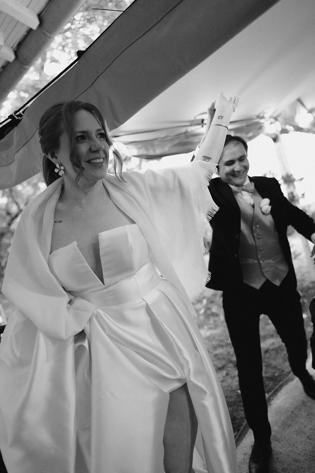 Un couple marié souriant, la femme avec un marié en costume noir, en train de faire un geste de célébration à une fête.