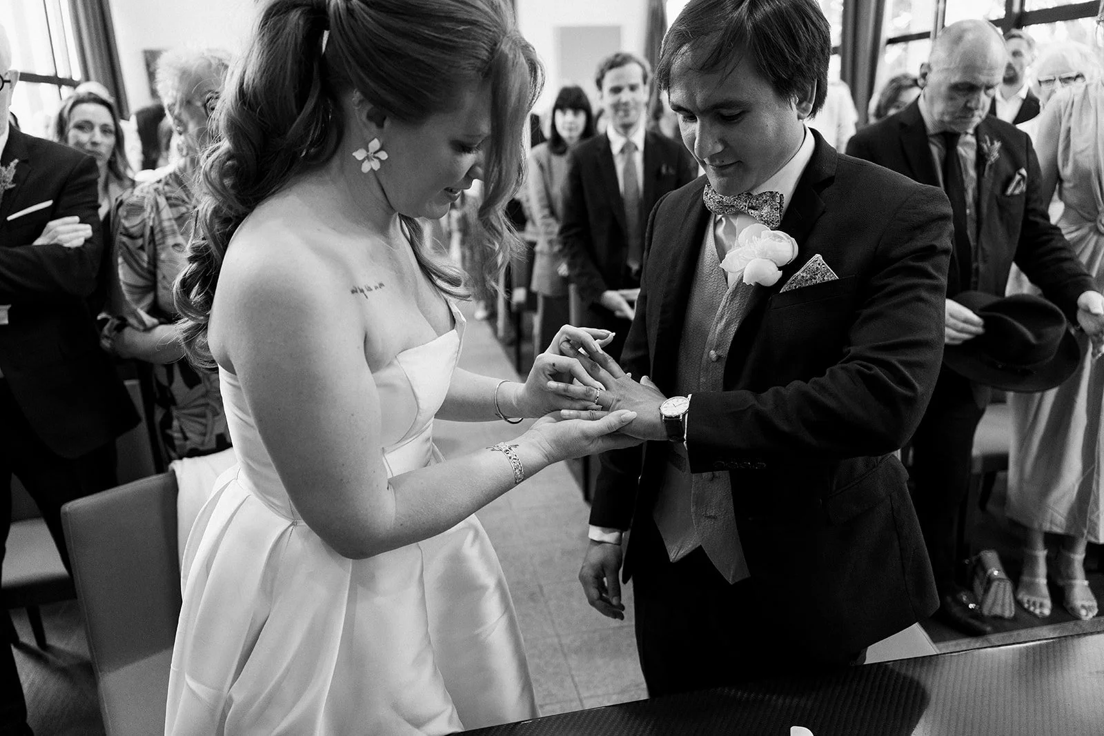 Un couple échange des alliances lors d'un mariage, avec des invités en arrière-plan.