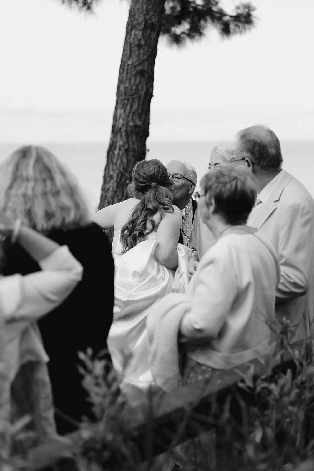 Groupe de personnes lors d'un mariage en plein air, en noir et blanc, avec un arbre en arrière-plan.