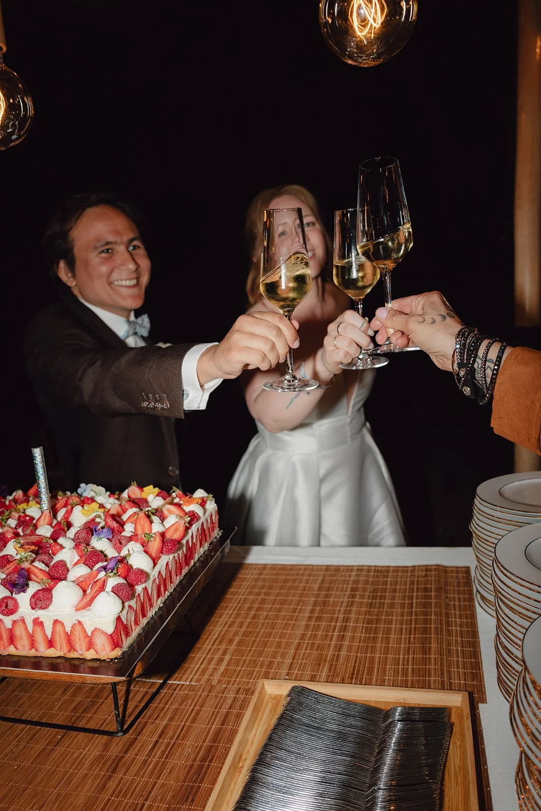 Deux personnes, un homme et une femme, trinquent avec des verres de champagne lors d'une célébration, avec un gâteau à la crème et aux fruits sur la table.