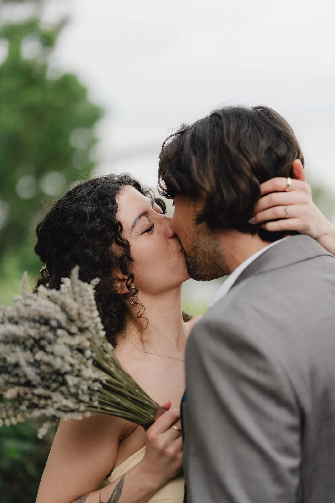 Un couple s'embrasse passionnément lors d'un mariage, la femme tient un bouquet de fleurs séchées.