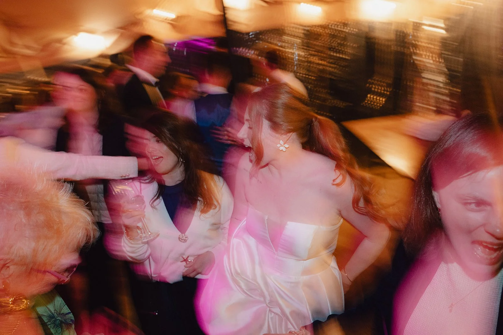 Groupe de personnes dansant et socialisant lors d'une fête ou d'un événement, avec des lumières chaudes et une ambiance animée.