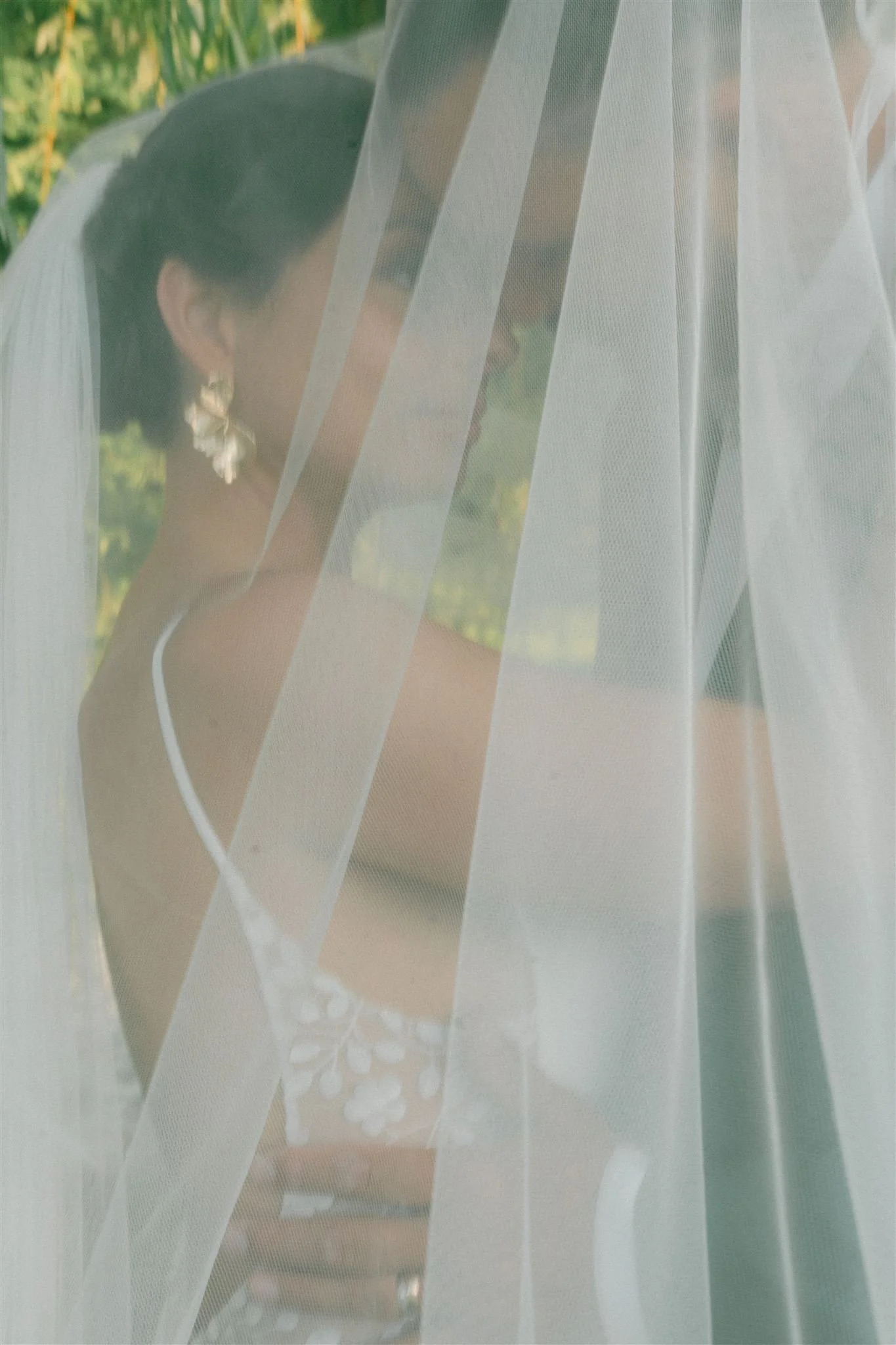 Une personne portant une robe blanche avec un voile, vue derrière une fenêtre en voile léger.