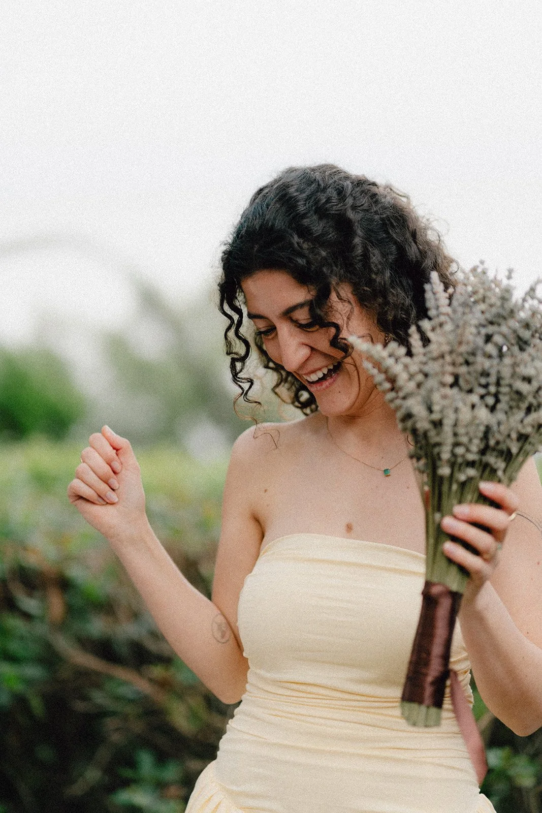 Femme souriante tenant un bouquet de fleurs dans un extérieur naturel.