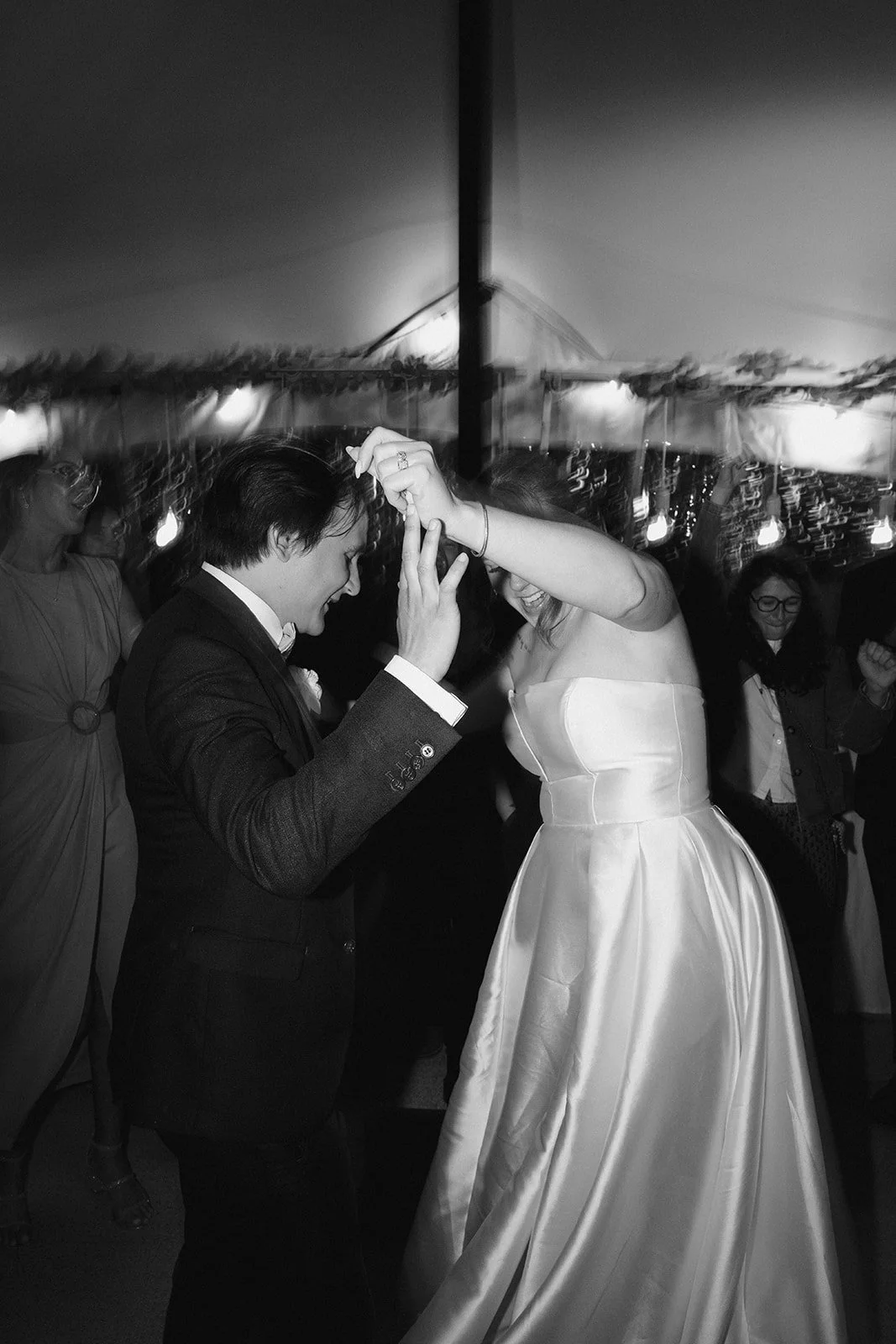 Un couple en train de danser lors d'une fête ou mariage, la femme porte une robe de mariée blanche, et l'homme porte un costume noir.