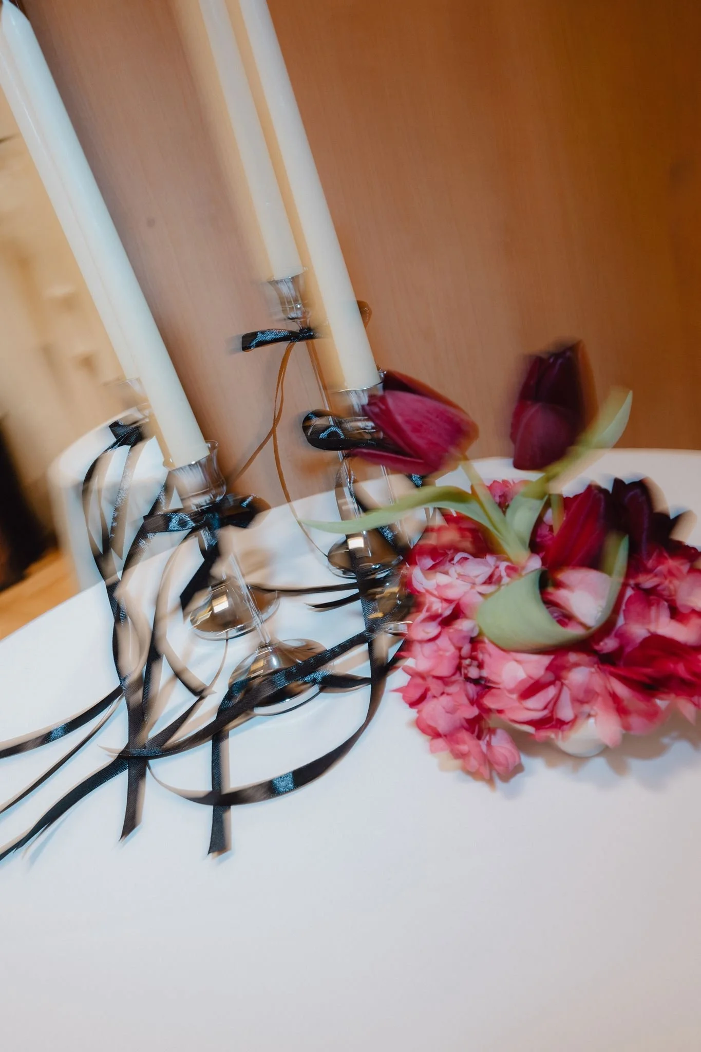 Composition florale avec roses rouges et fleurs roses, plateforme blanche décorée avec des rubans noirs.