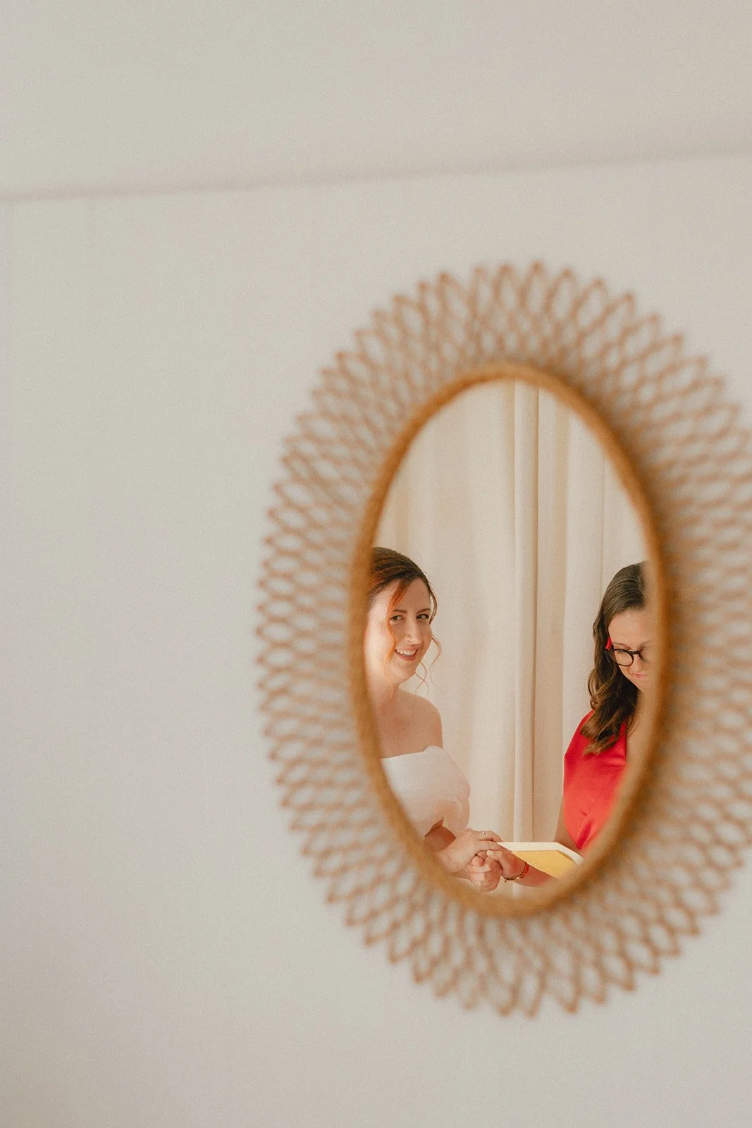 Photo prise à travers un miroir en rotin de la mariée et sa témoin
