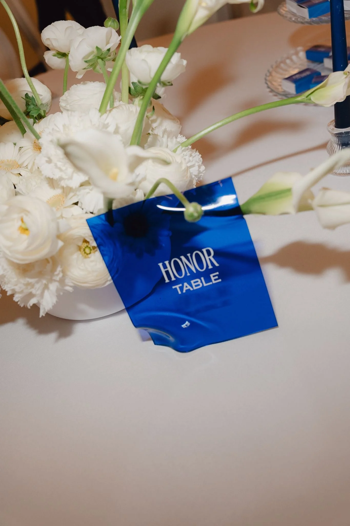 Un bouquet de fleurs blanches sur une table avec un badge bleu où il est écrit 'HONOR TABLE'.