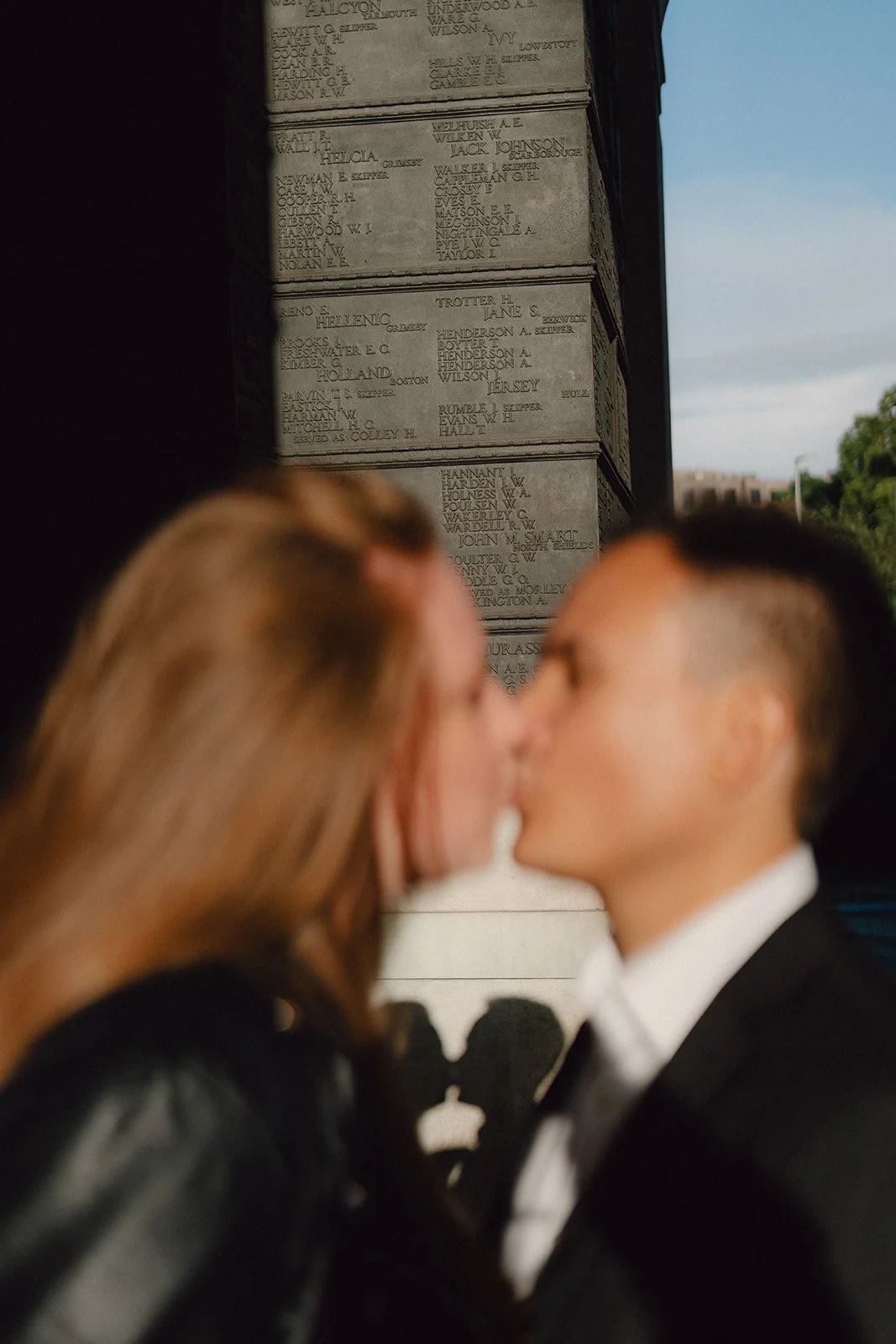 Deux personnes s'embrassent devant un mur commémoratif avec des noms gravés, lors d'une cérémonie.