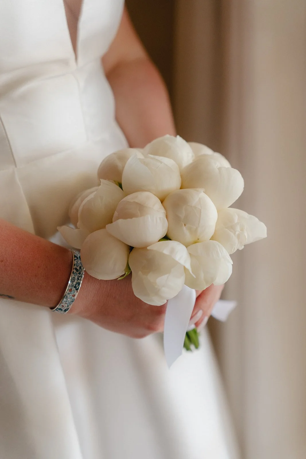 Une personne en robe blanche tient un bouquet de roses blanches lors d'un mariage.
