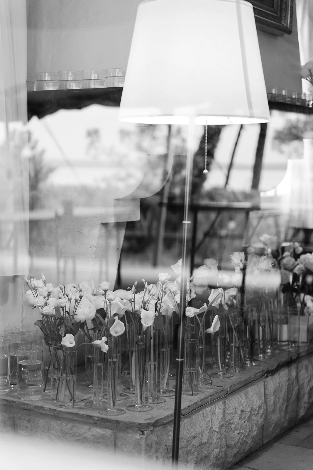 Une vitrine avec des fleurs blanches dans des vases en verre, une lampe de sol blanche et des meubles en arrière-plan.